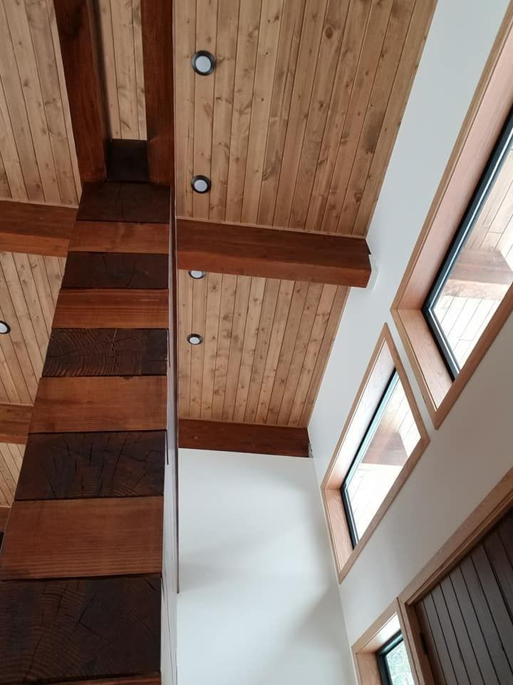 Looking up at the ceiling of a house with wooden beams and windows.