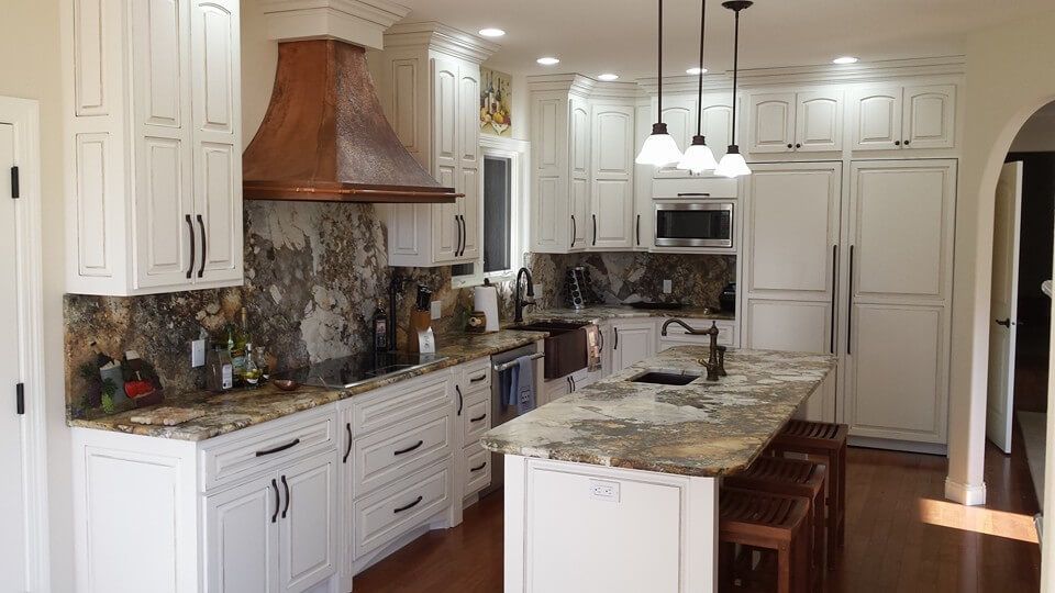 A kitchen with white cabinets , granite counter tops , and a large island.