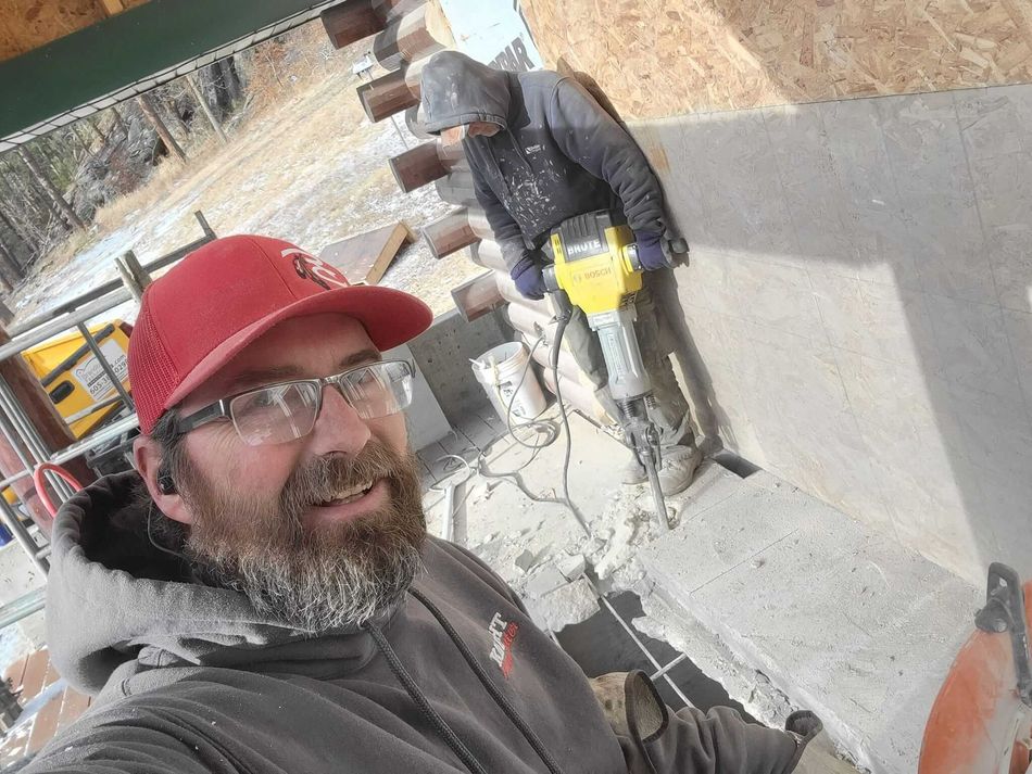 A man wearing a red hat and glasses is standing next to another man holding a hammer.
