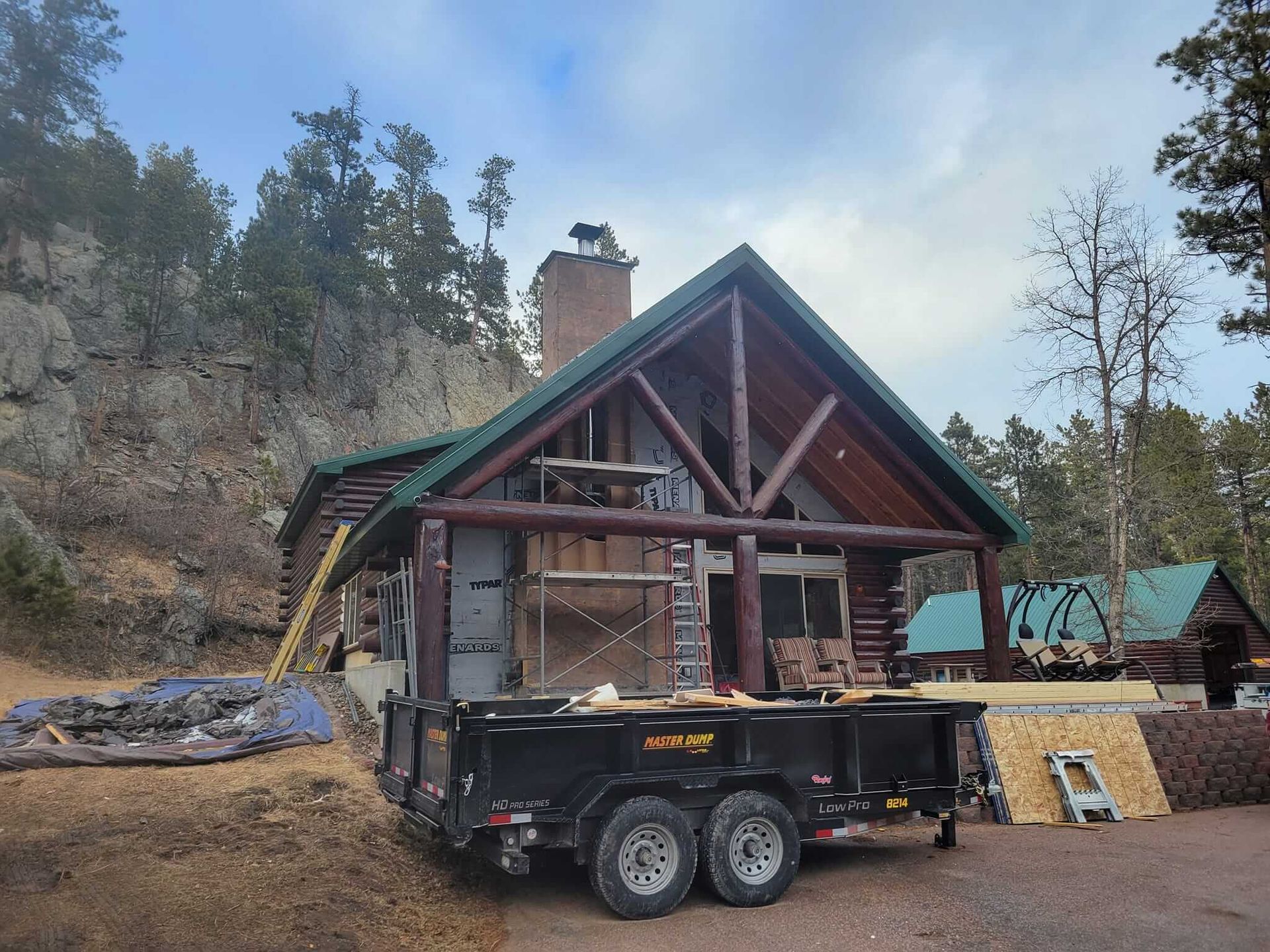 A log cabin is being built and a trailer is parked in front of it