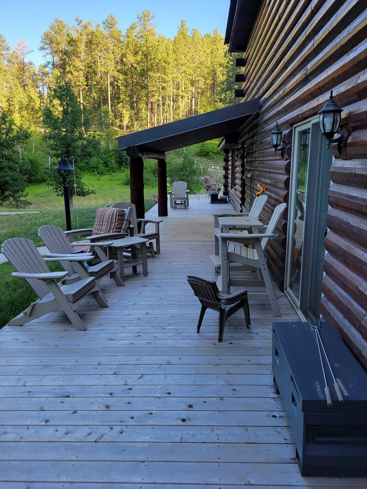 A wooden deck with chairs and tables on it in front of a log cabin.