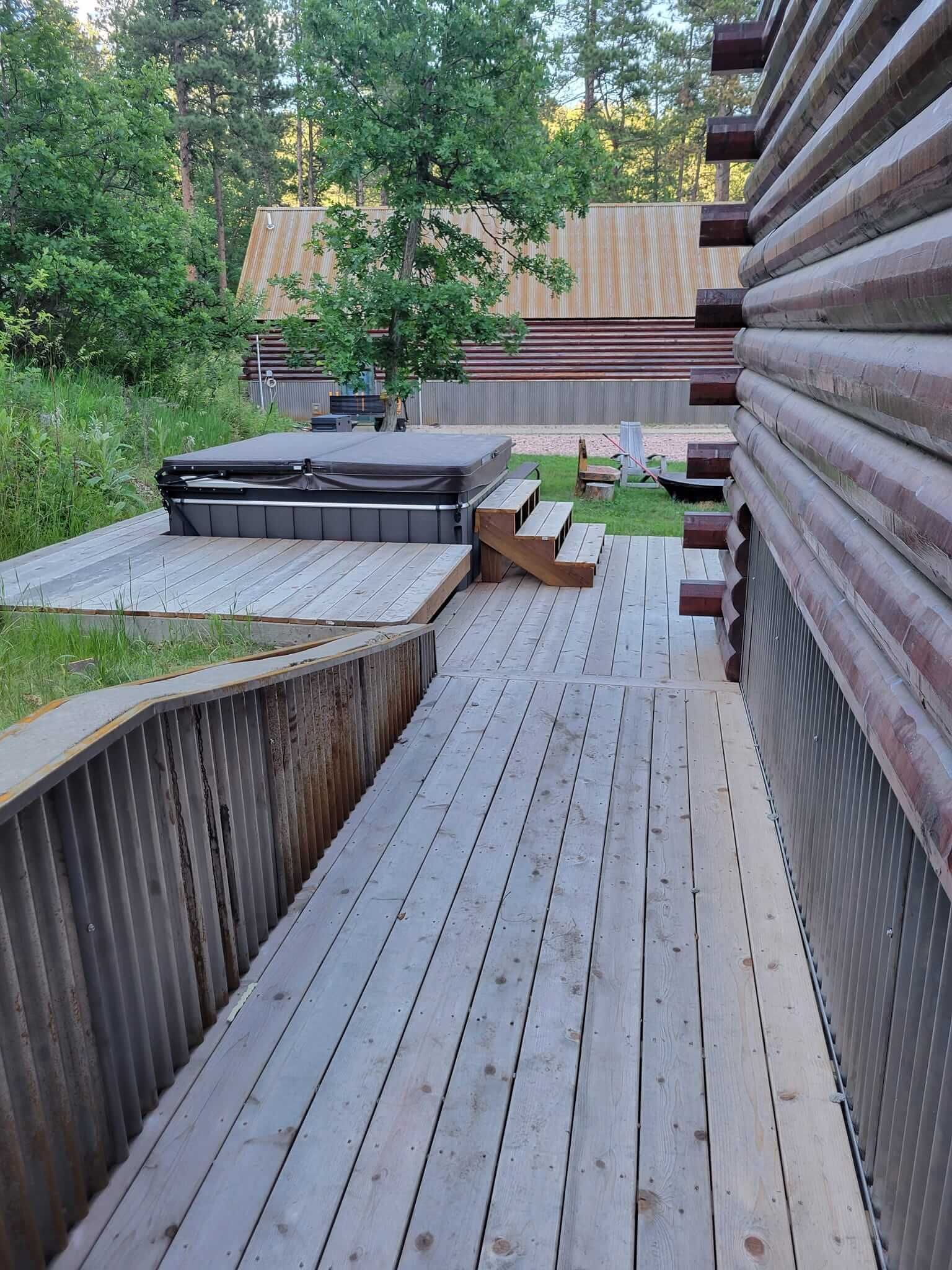 A wooden walkway leading to a hot tub in the backyard of a log cabin.