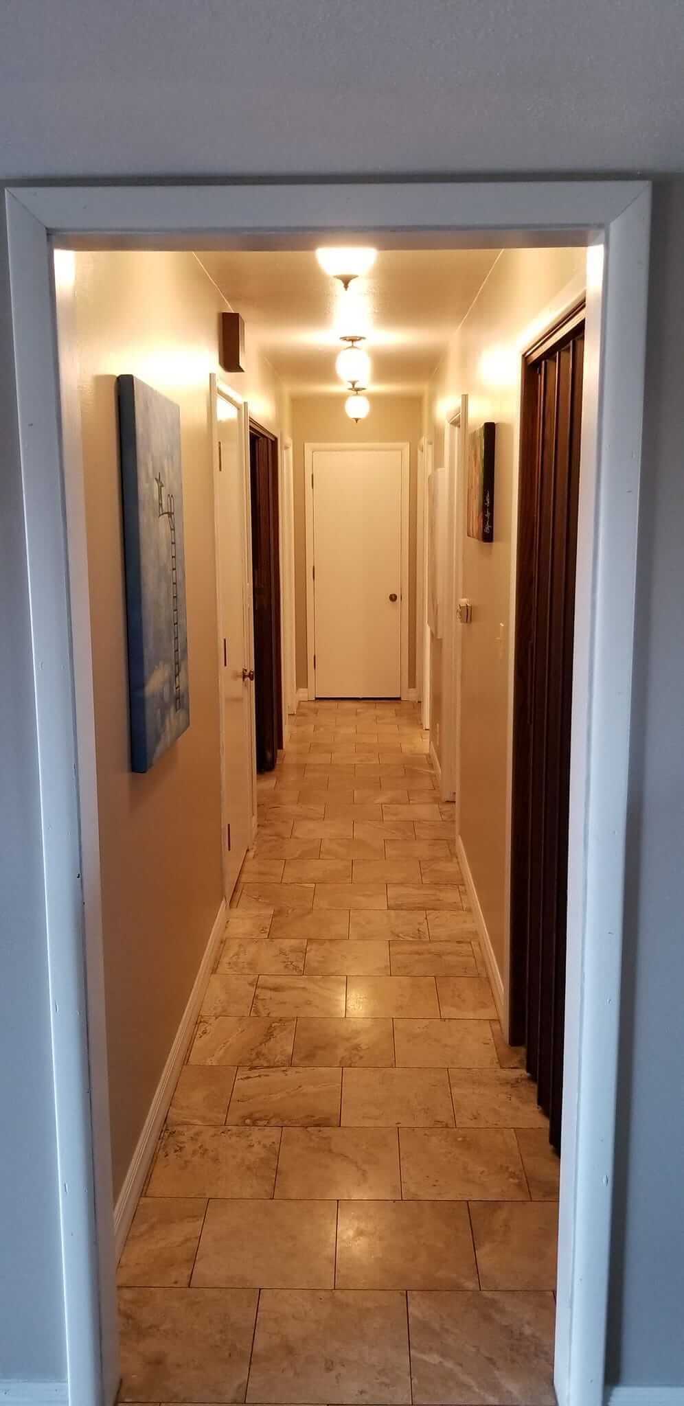 A long hallway with a door open and a painting on the wall.