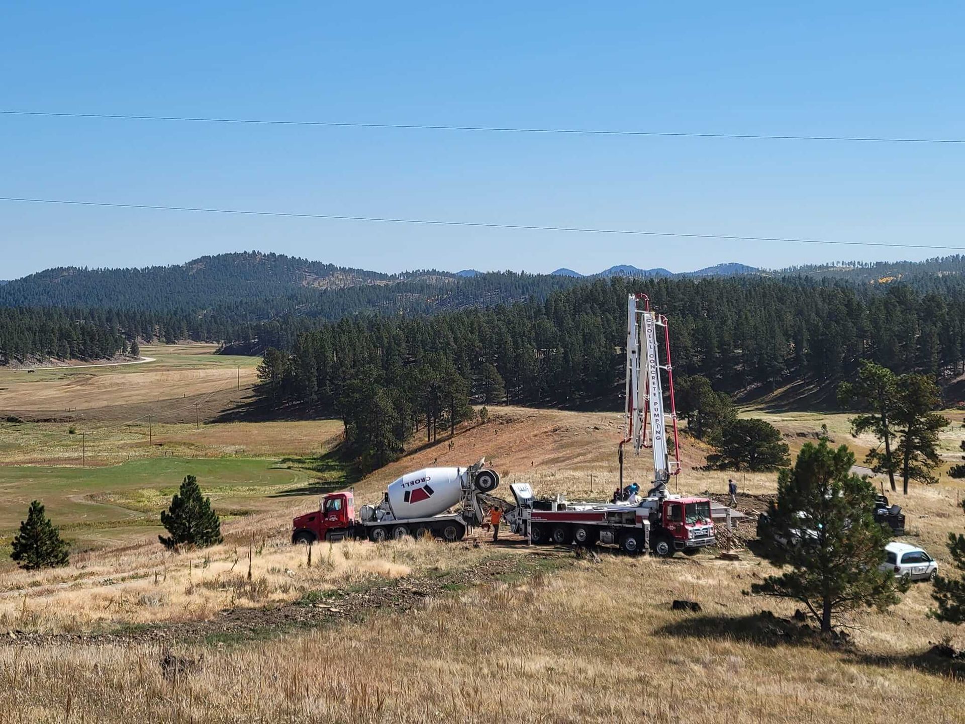 A concrete mixer truck is driving down a dirt road in a field.