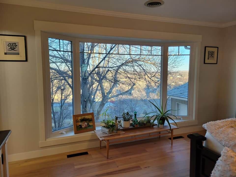 A living room with a large window and a bench with plants on it.