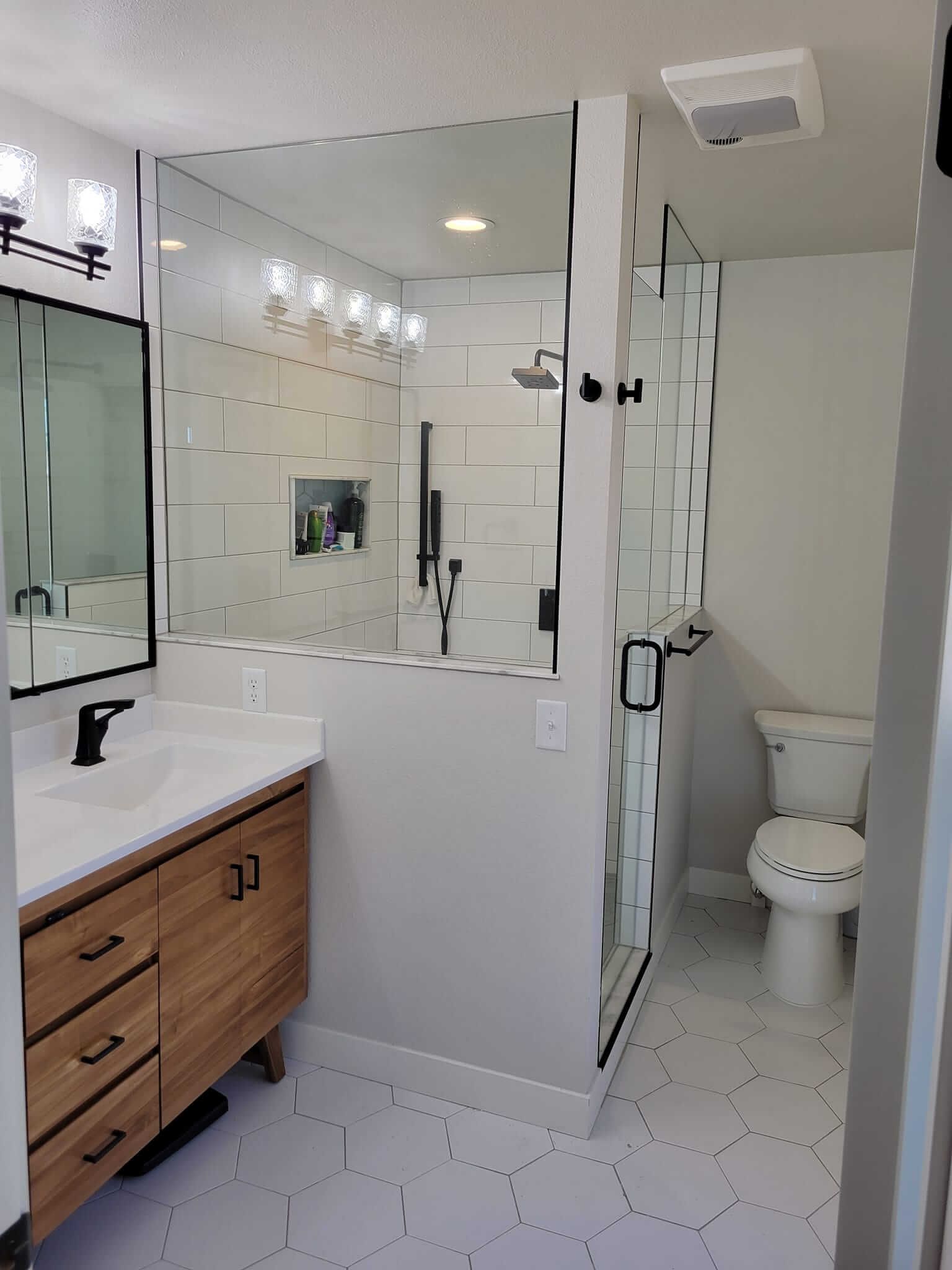 A bathroom with a sink , toilet , shower and mirror.