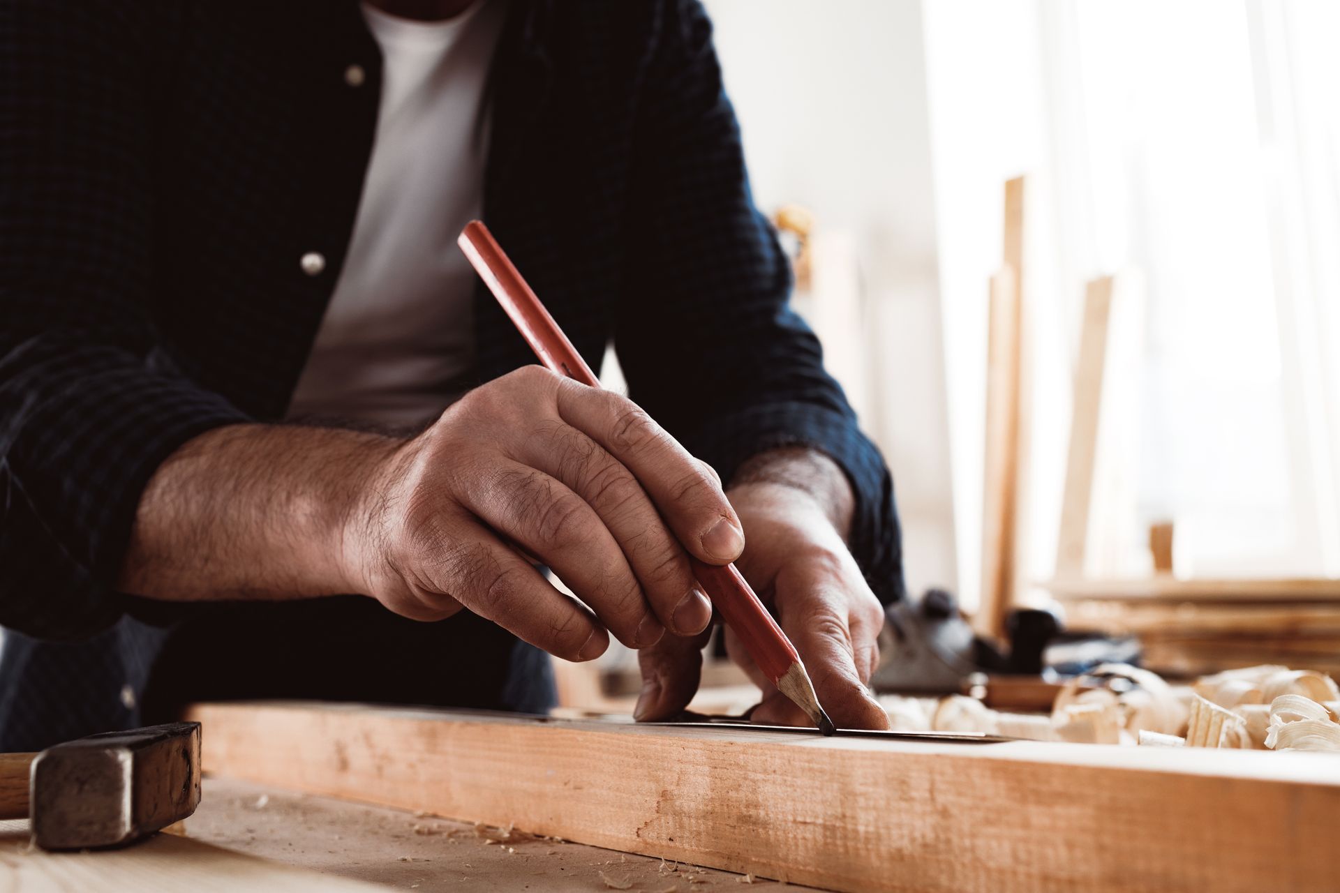 Carpenter marking a wooden plank with a pencil and ruler, workshop setting.