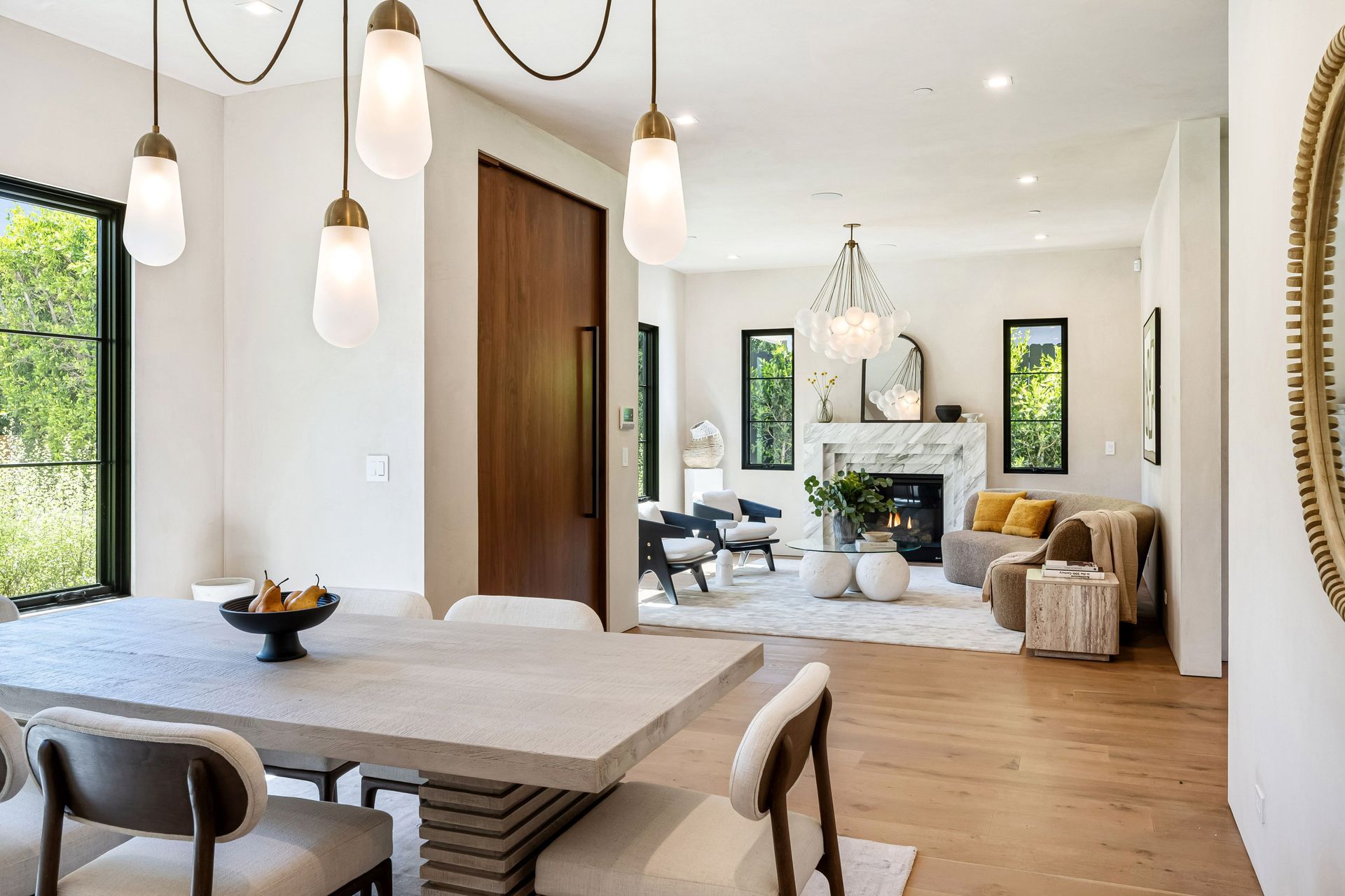 Modern dining and living room with a long dining table, fireplace, and large windows.