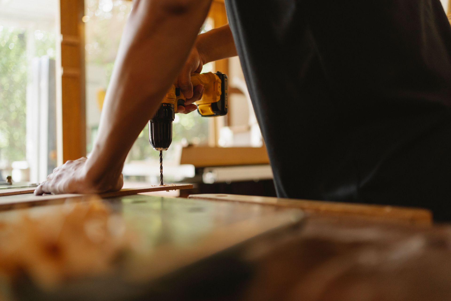 Person using a drill press in a workshop, with a wooden workbench in the foreground