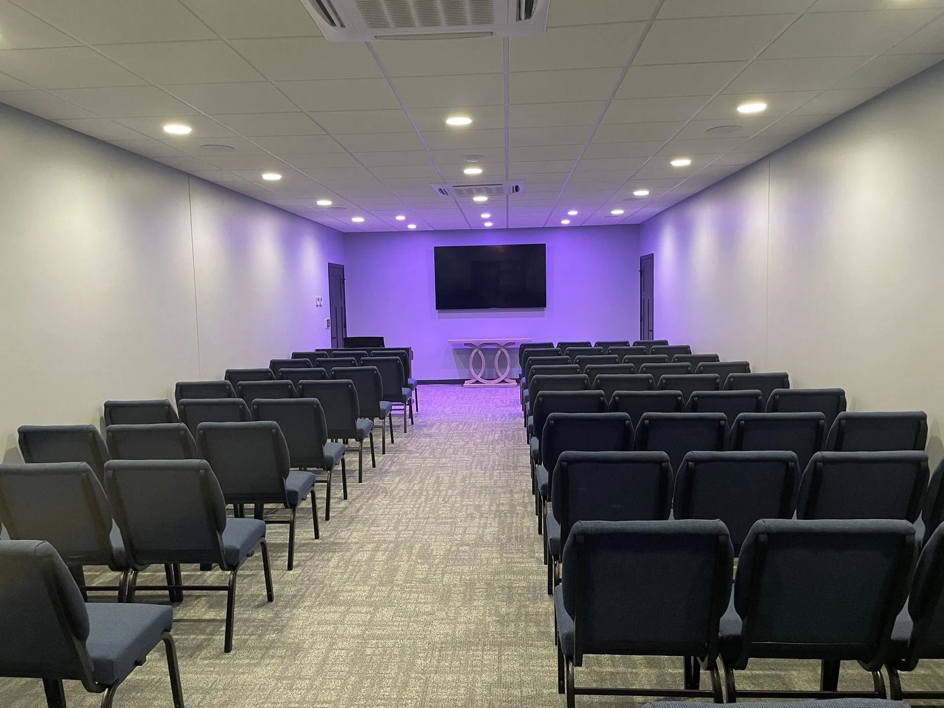 Rows of blue chairs face a large screen in a room with gray walls and a light-colored carpet.