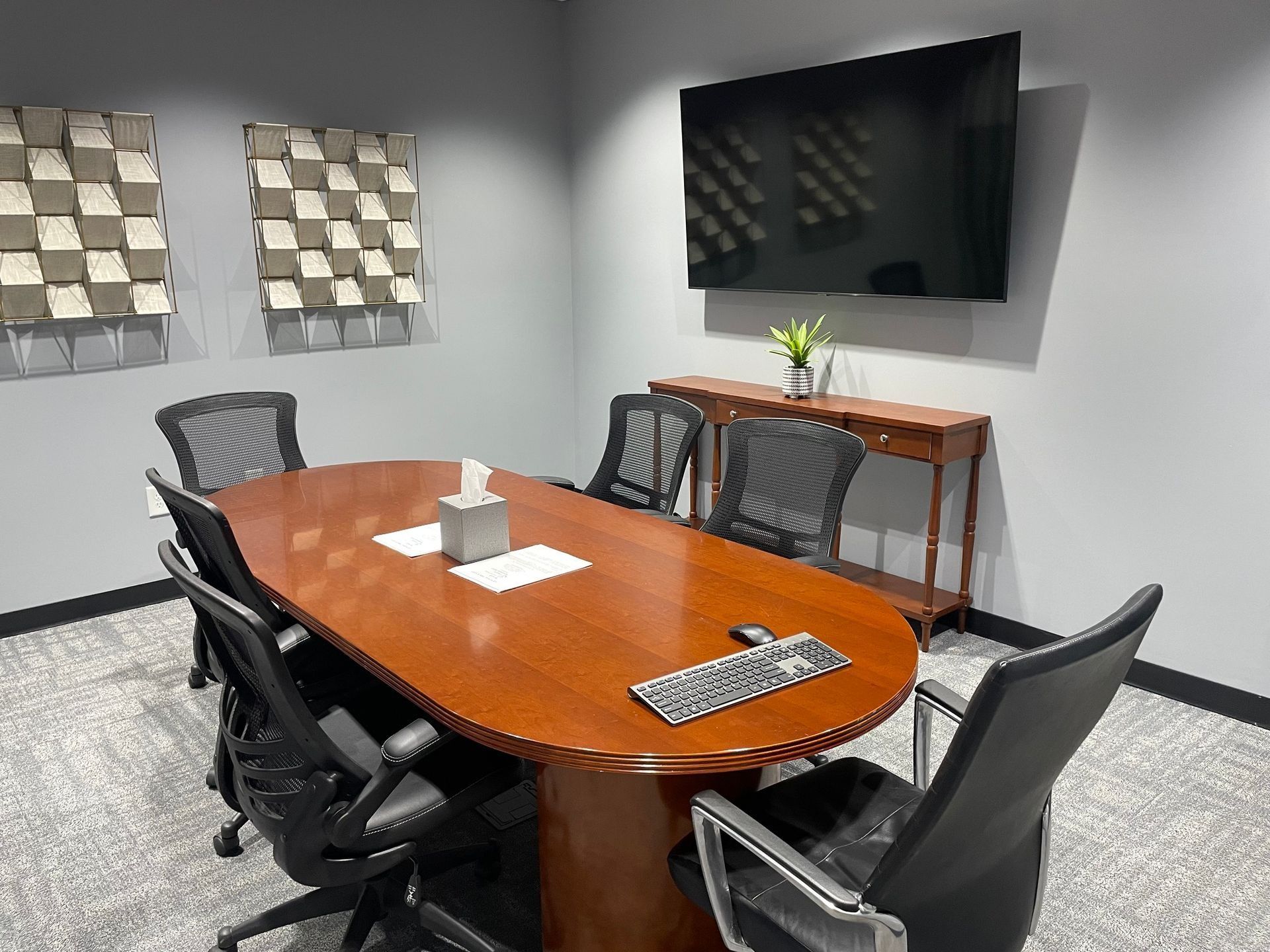 Conference room with oval wooden table, black chairs, TV, and decorative wall art.