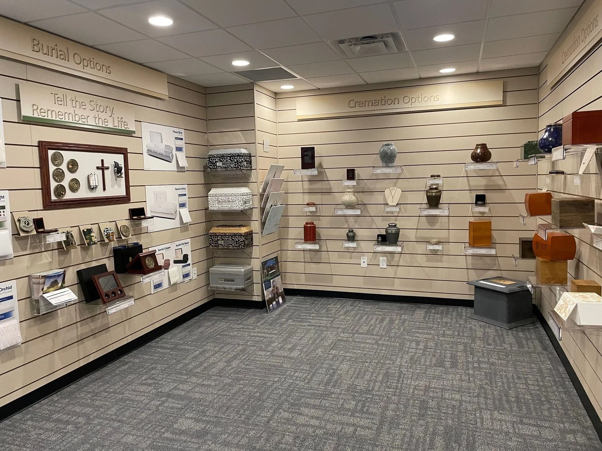 Interior of a showroom displaying urns and memorial items on slotted walls; neutral tones.