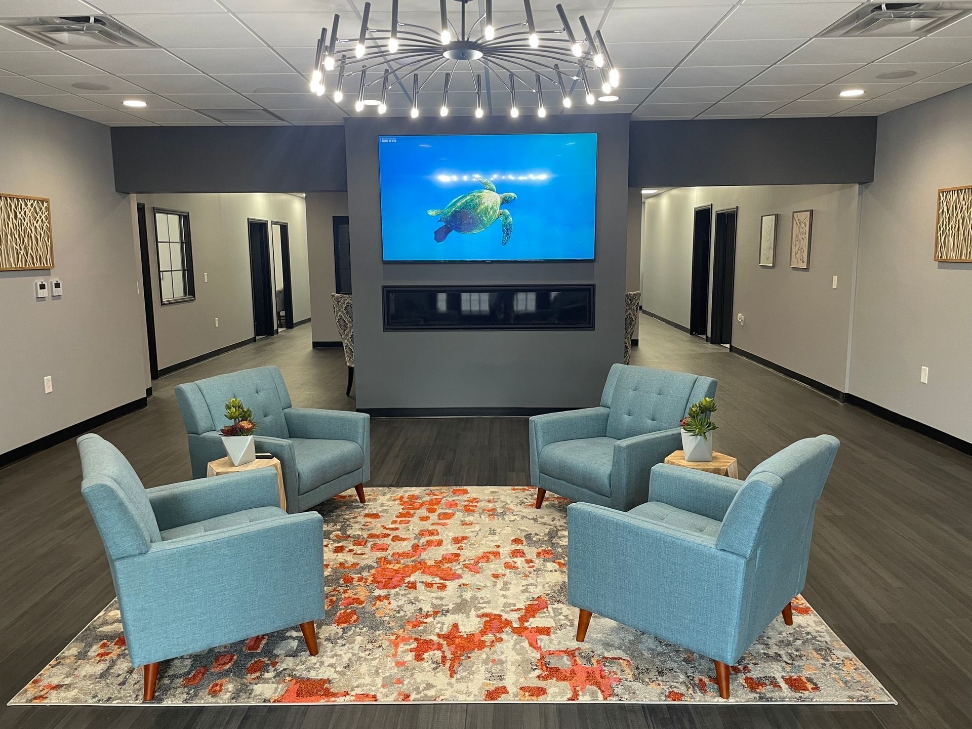 Waiting room with blue chairs, rug, television, and decorative lighting.