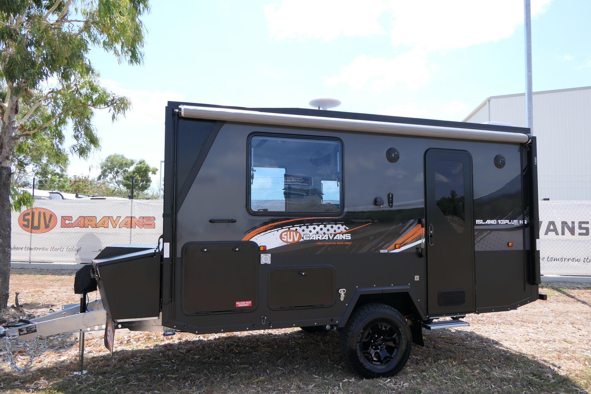 A black trailer is parked in a grassy area in front of a building.