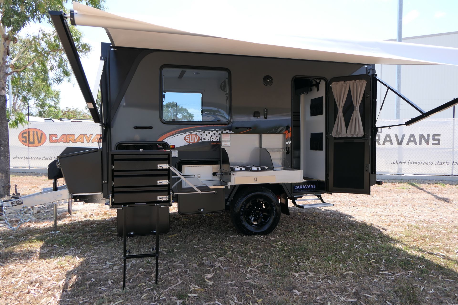 A camper trailer with a ladder and awning is parked in a field.