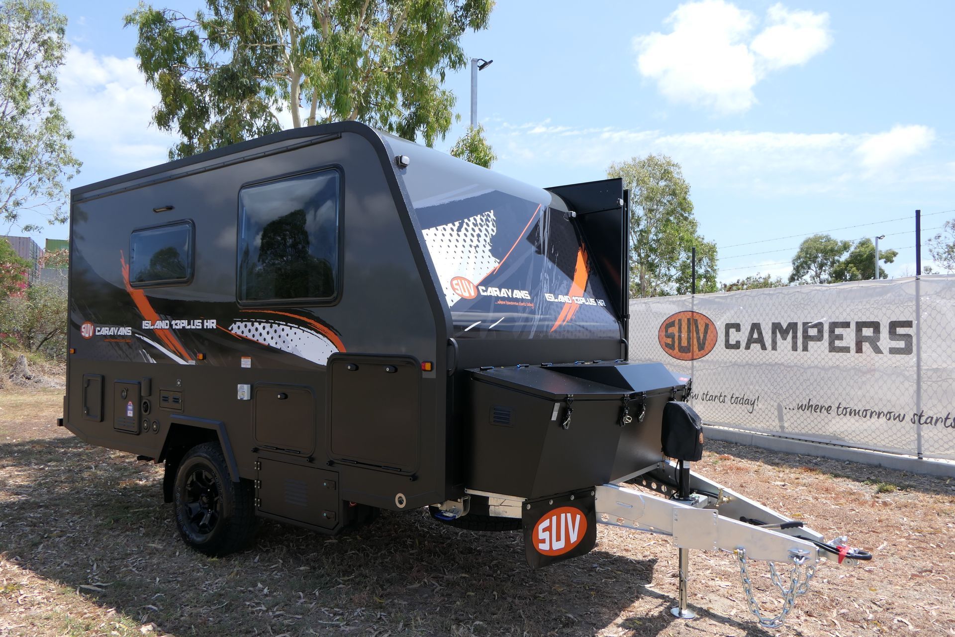 A black camper trailer is parked in front of a sign that says suv campers.