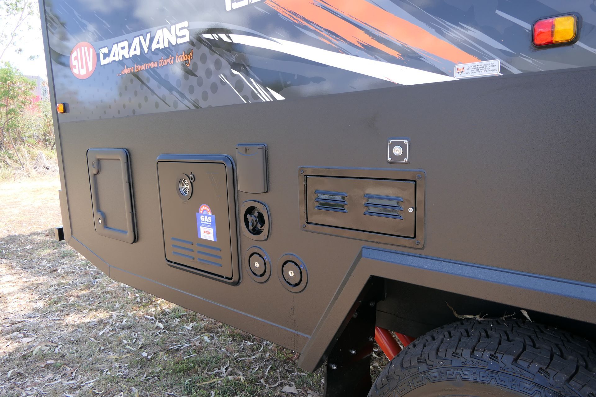 A black caravan is parked in a dirt field.