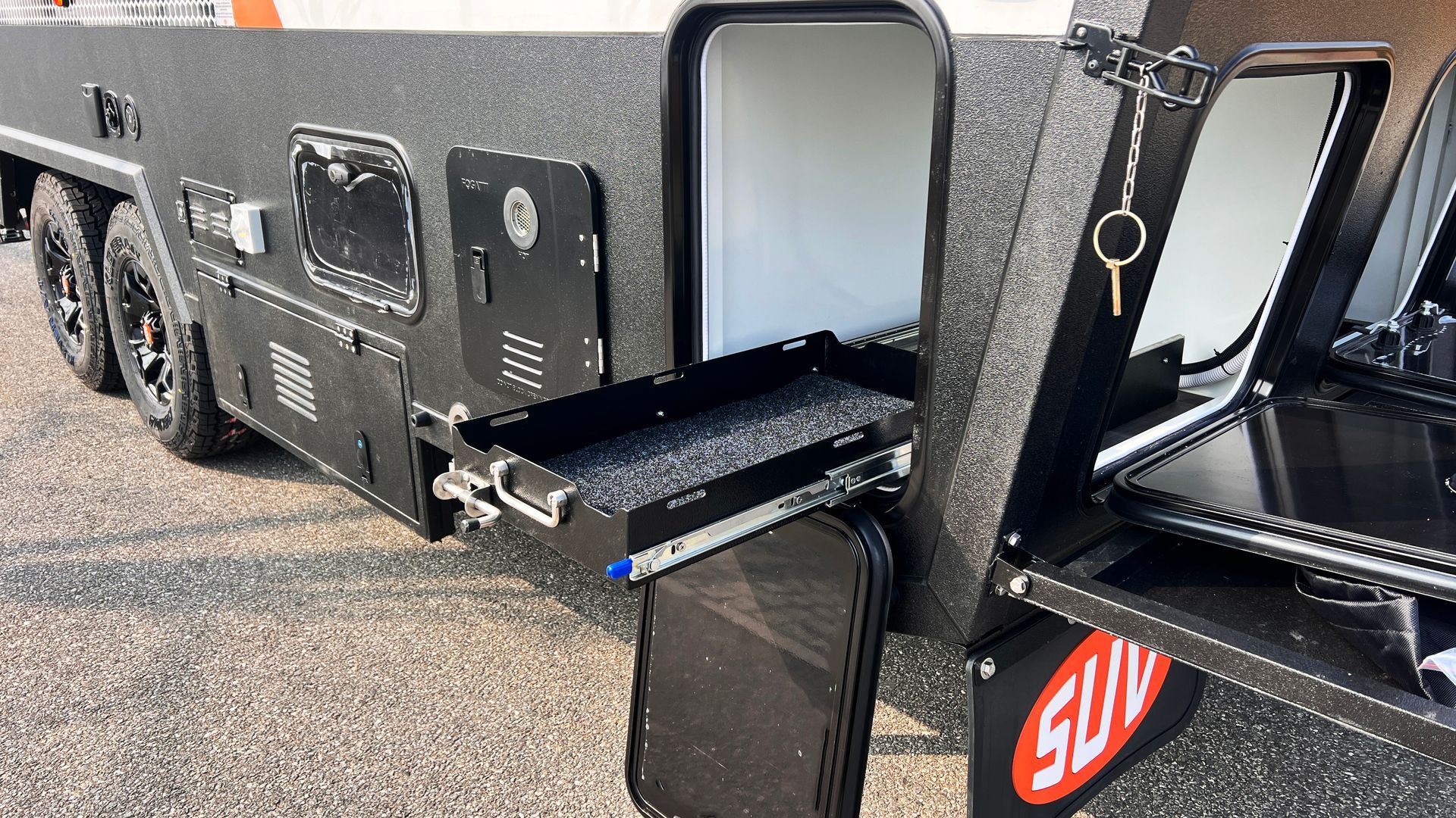 A black trailer with a red suv logo on the side is parked on the side of the road.