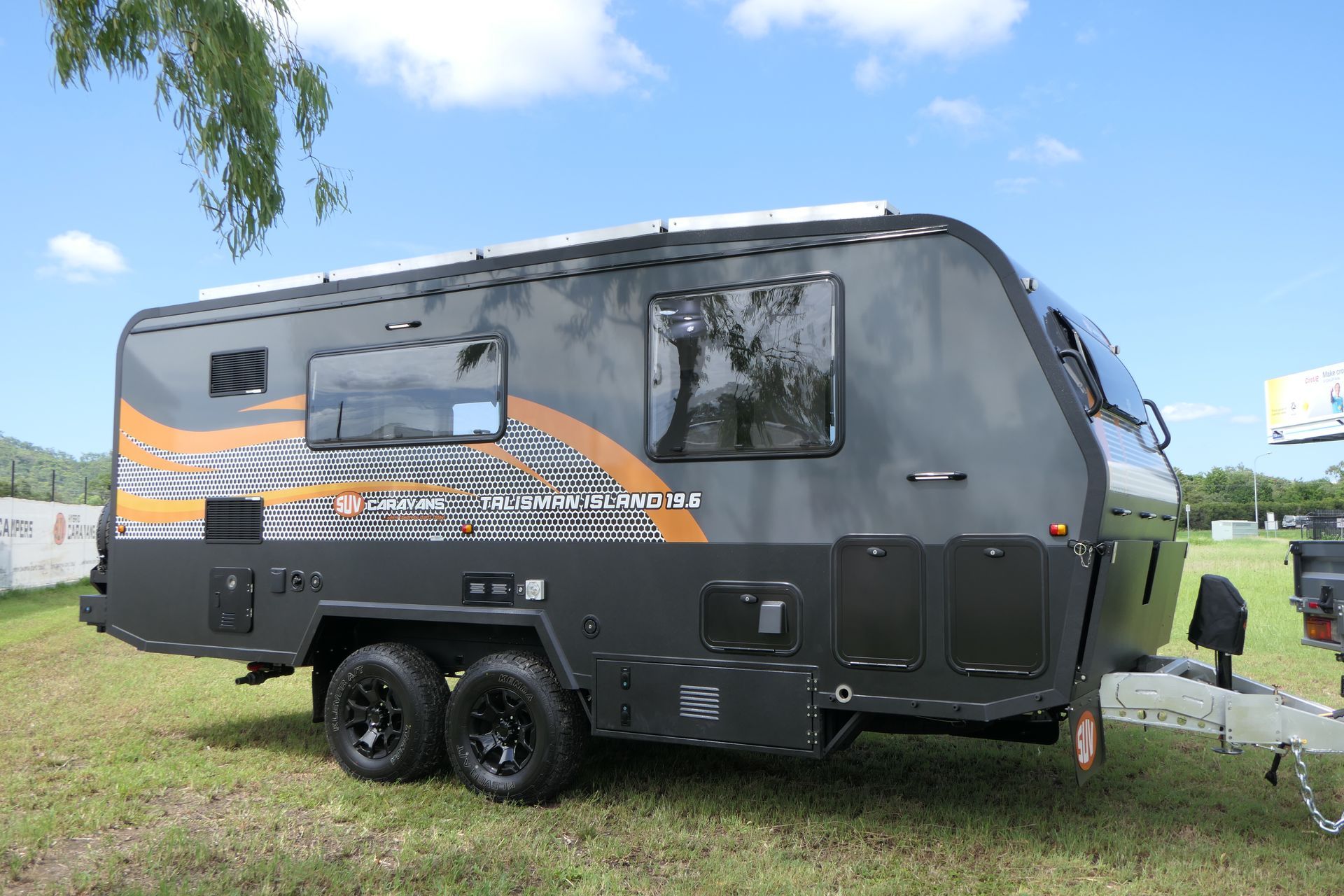 A black and orange camper trailer is parked in a grassy field.
