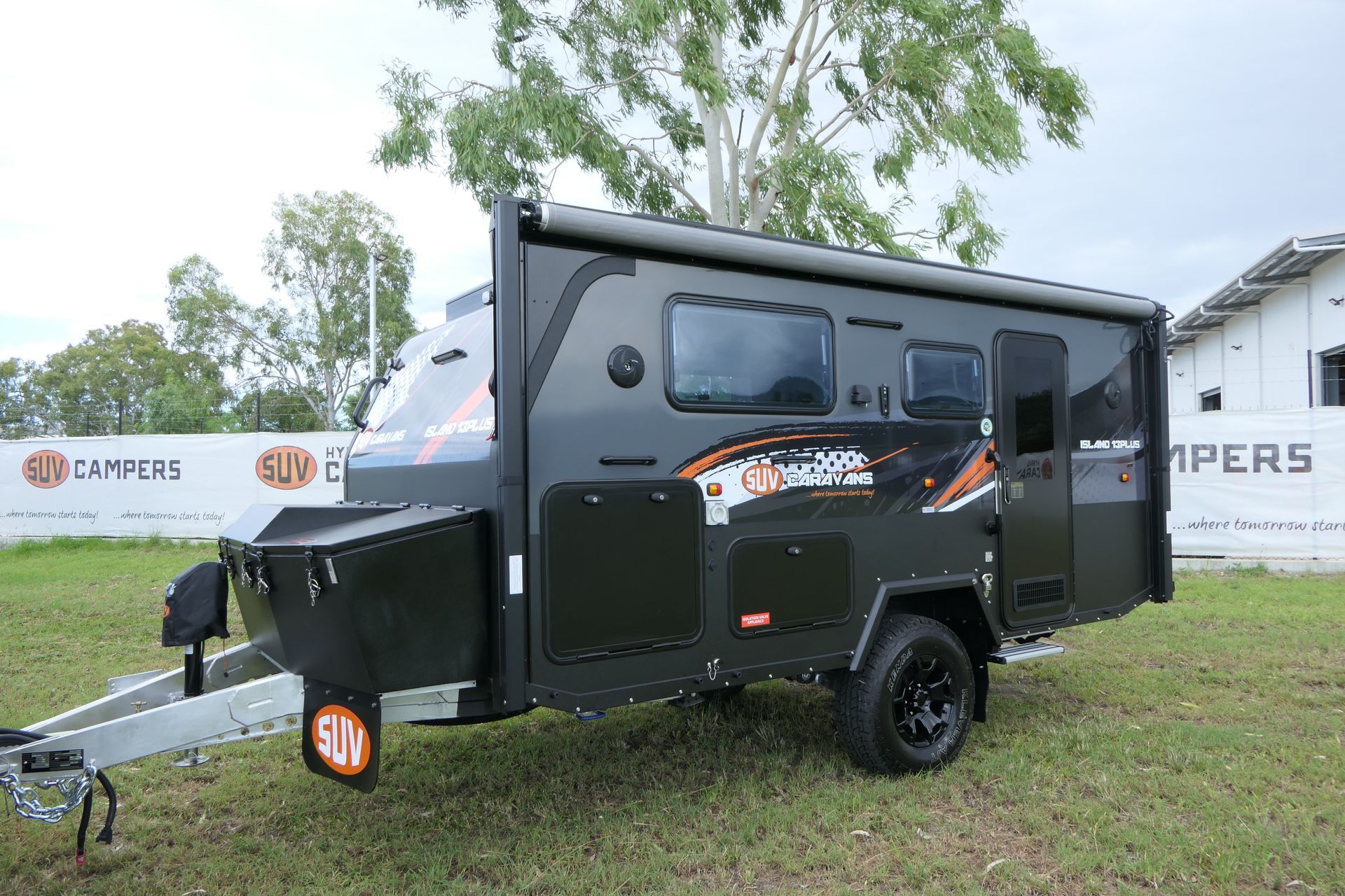 A black trailer is parked in a grassy field in front of a building.