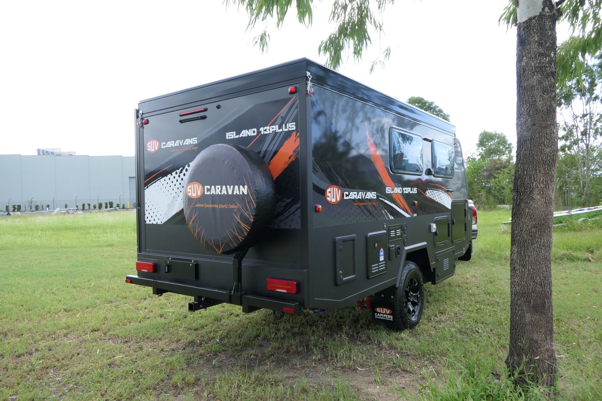 A black camper trailer is parked in a grassy field next to a tree.