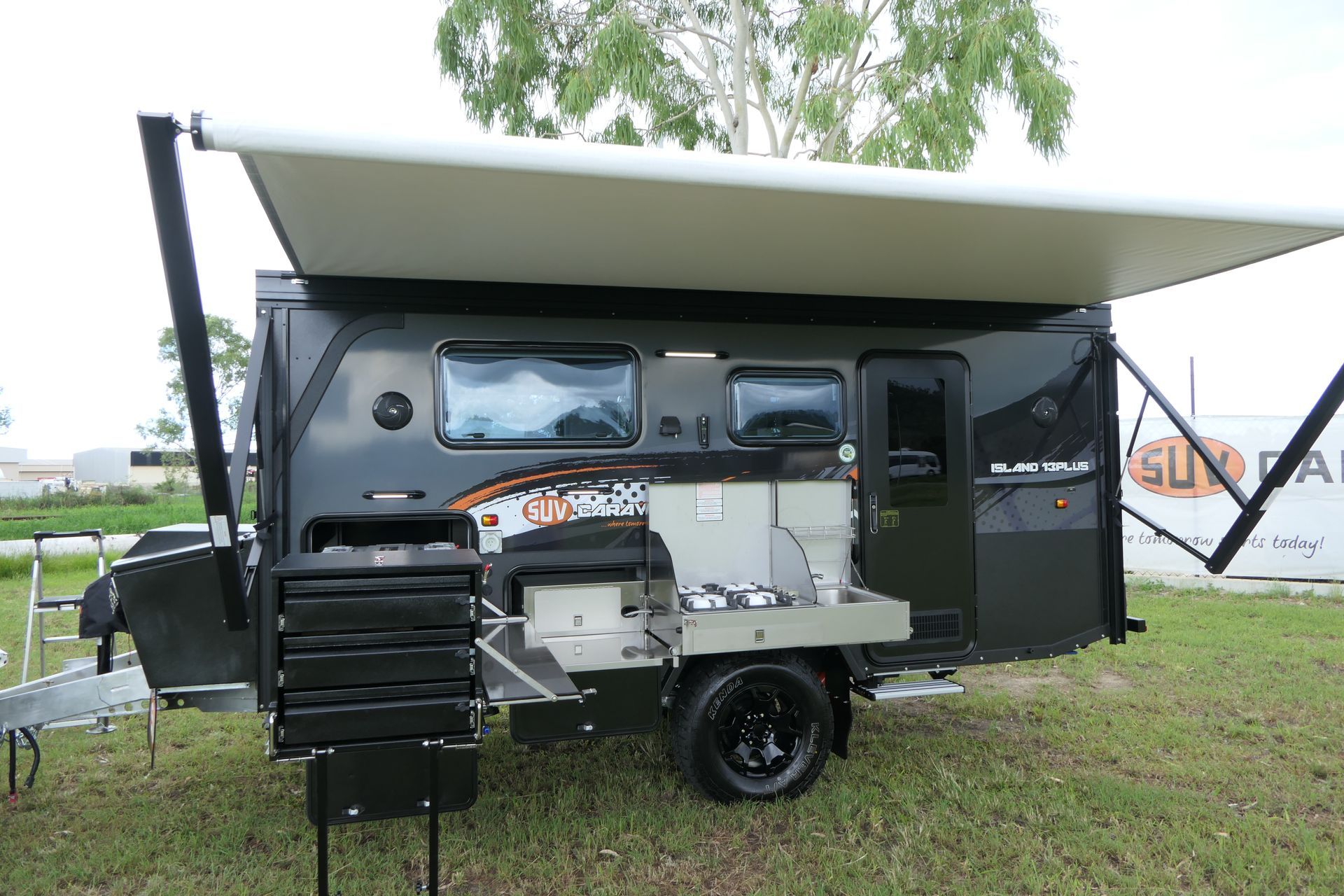 A black trailer with a white awning is parked in a grassy field.