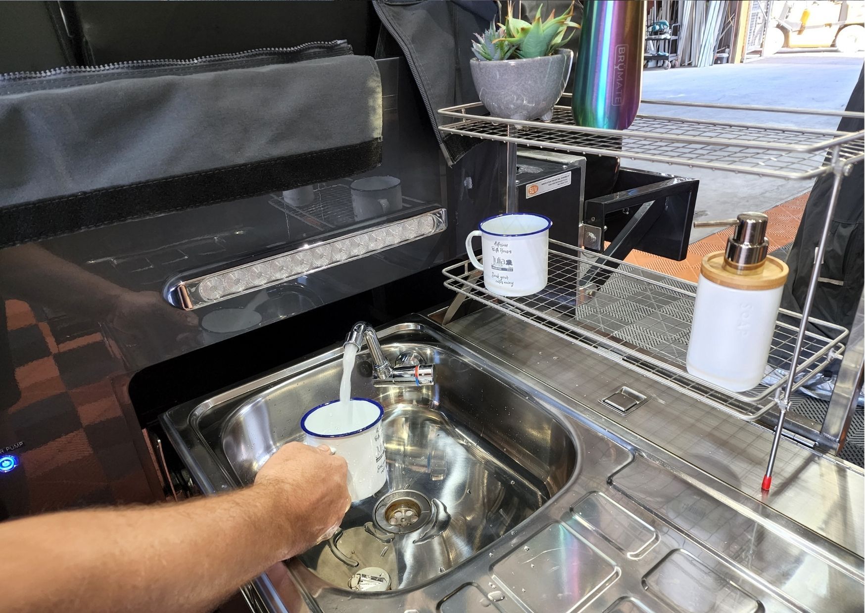 A person is washing a cup in a sink in a kitchen.