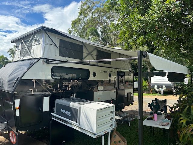 A camper trailer with a tent on top of it is parked next to a table.