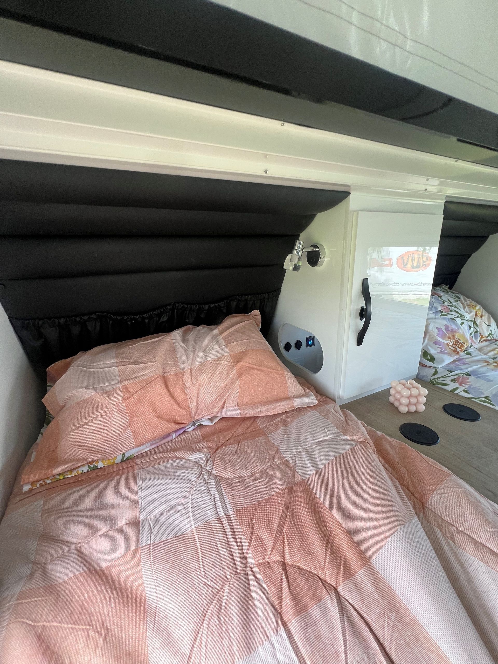 A bed with a pink comforter and pillows in a camper.