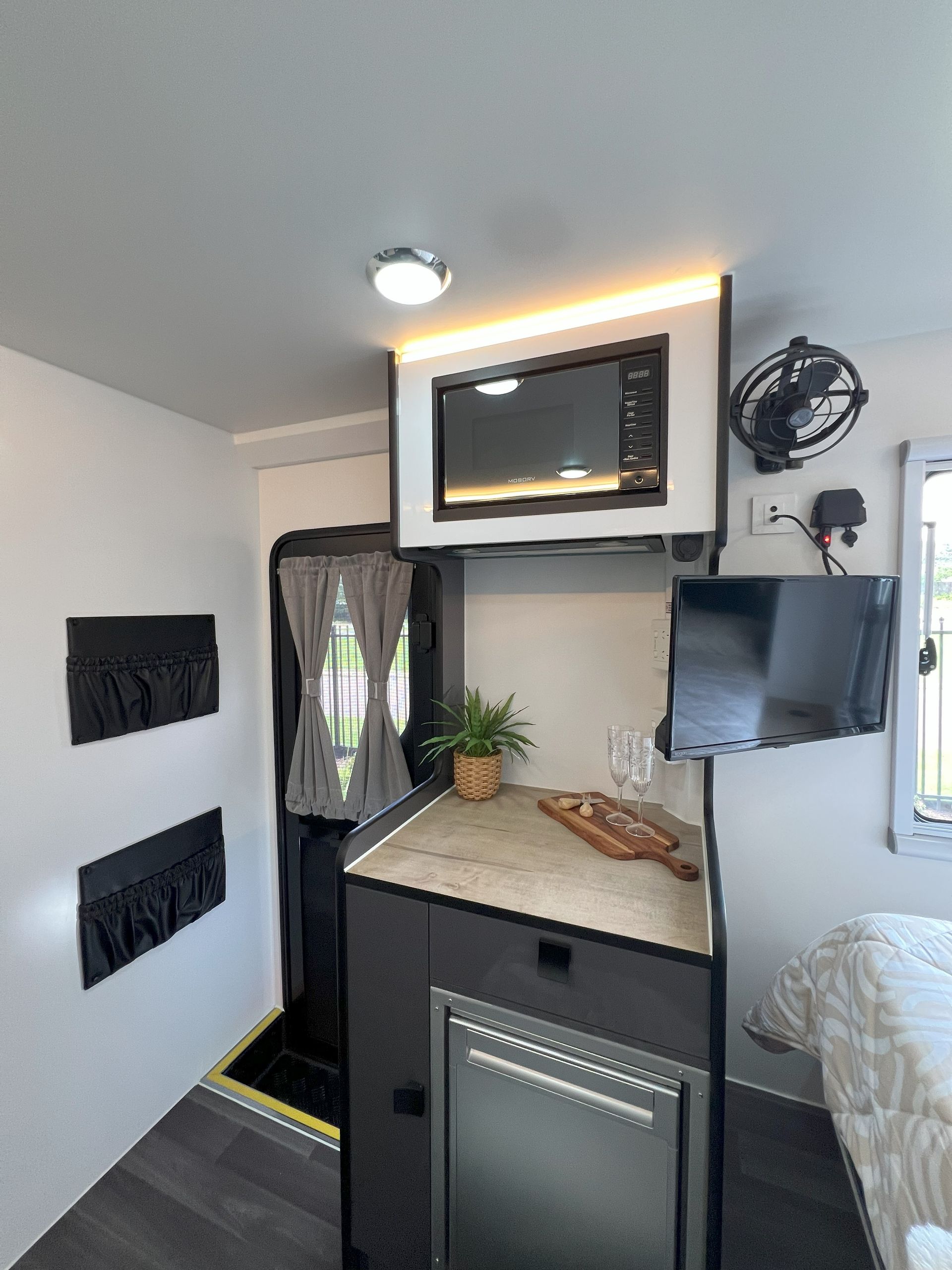 A kitchen in a camper with a microwave , refrigerator , and television.