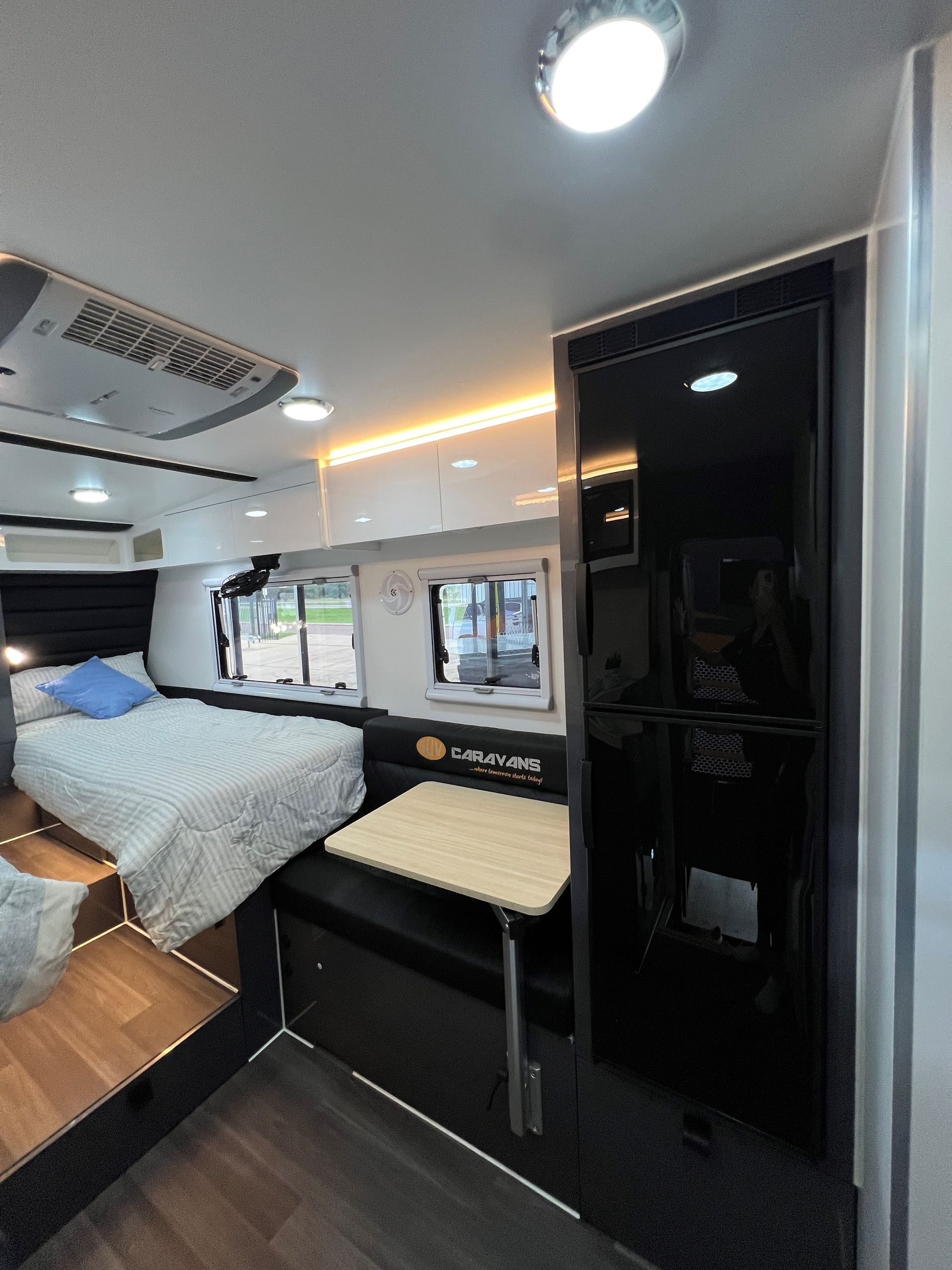 A bedroom in a camper with a bed , table and mirror.