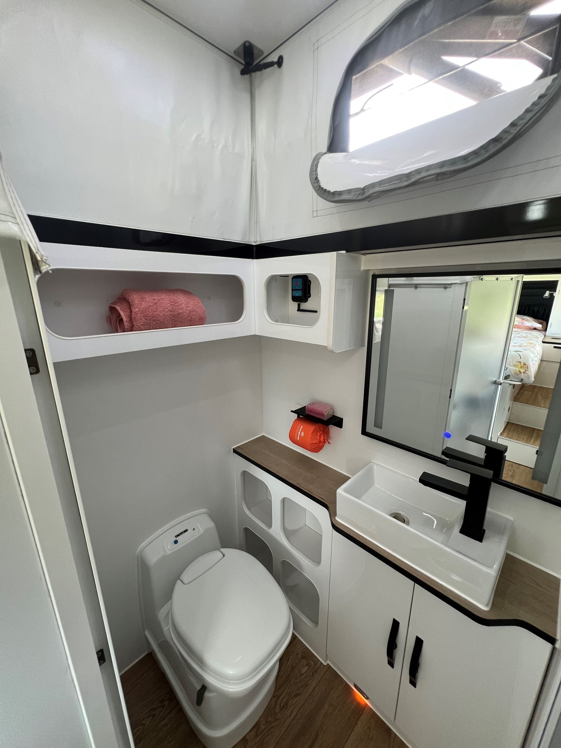 A bathroom in a camper with a toilet , sink and mirror.
