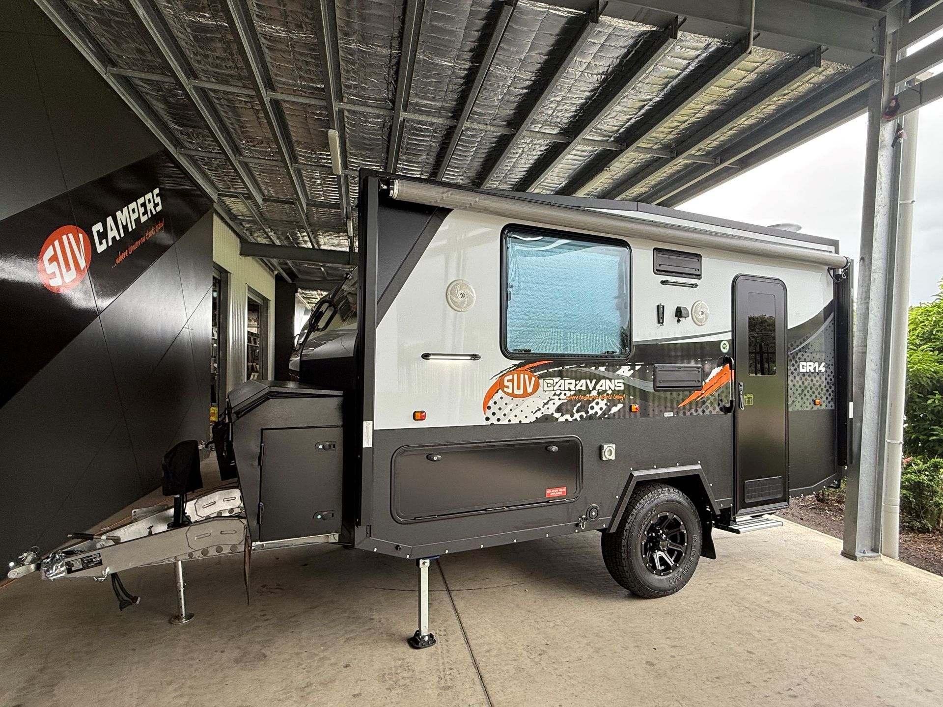 A camper trailer is parked under a canopy in a parking lot.