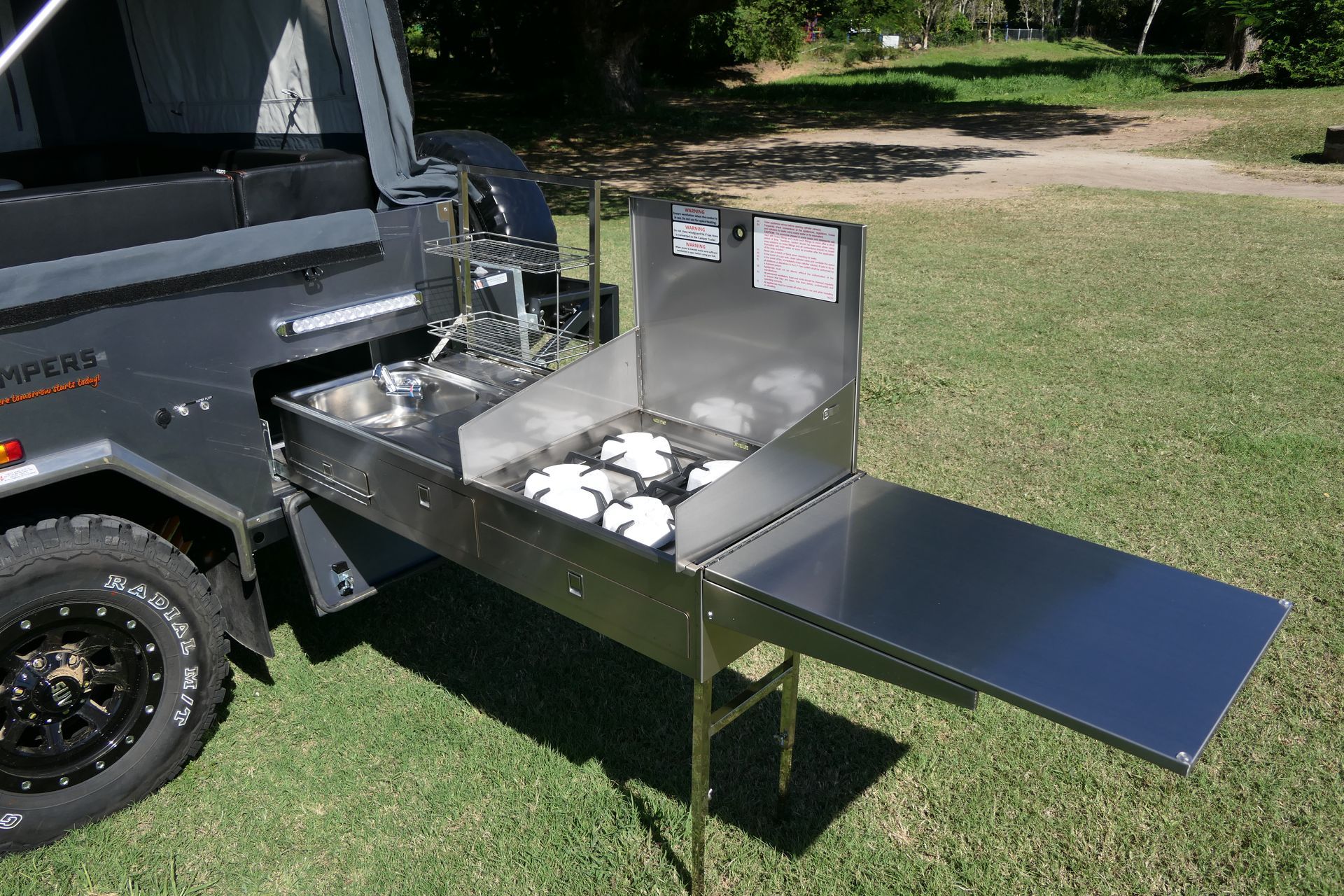 A stainless steel kitchen is attached to the side of a vehicle.