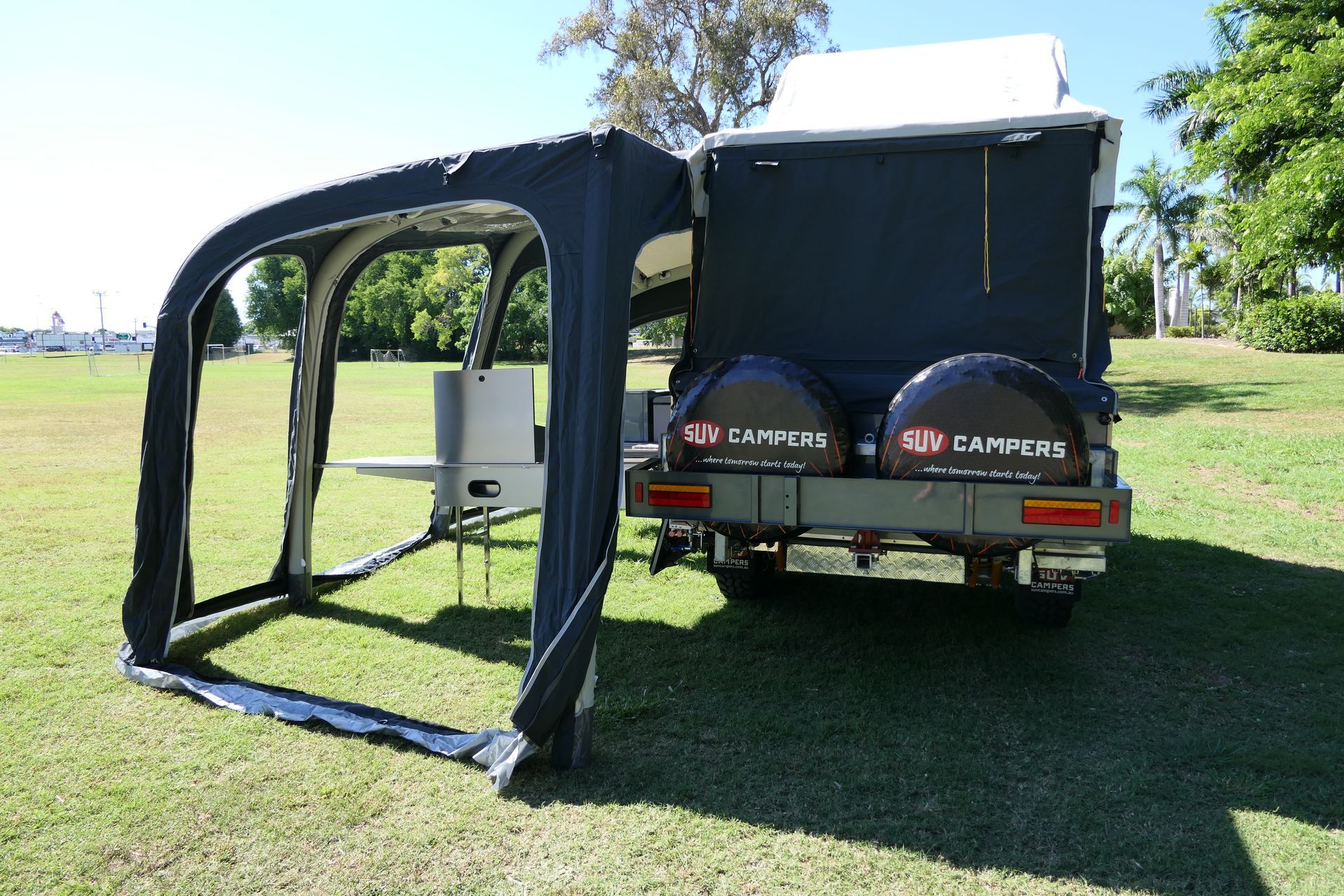 A camper is parked in a grassy field with a tent attached to it.