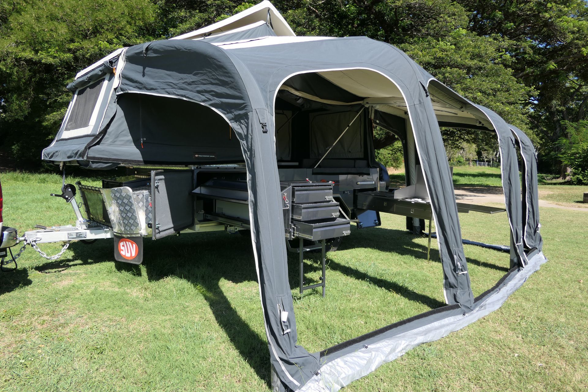 A trailer with a tent attached to it is parked in a grassy field.
