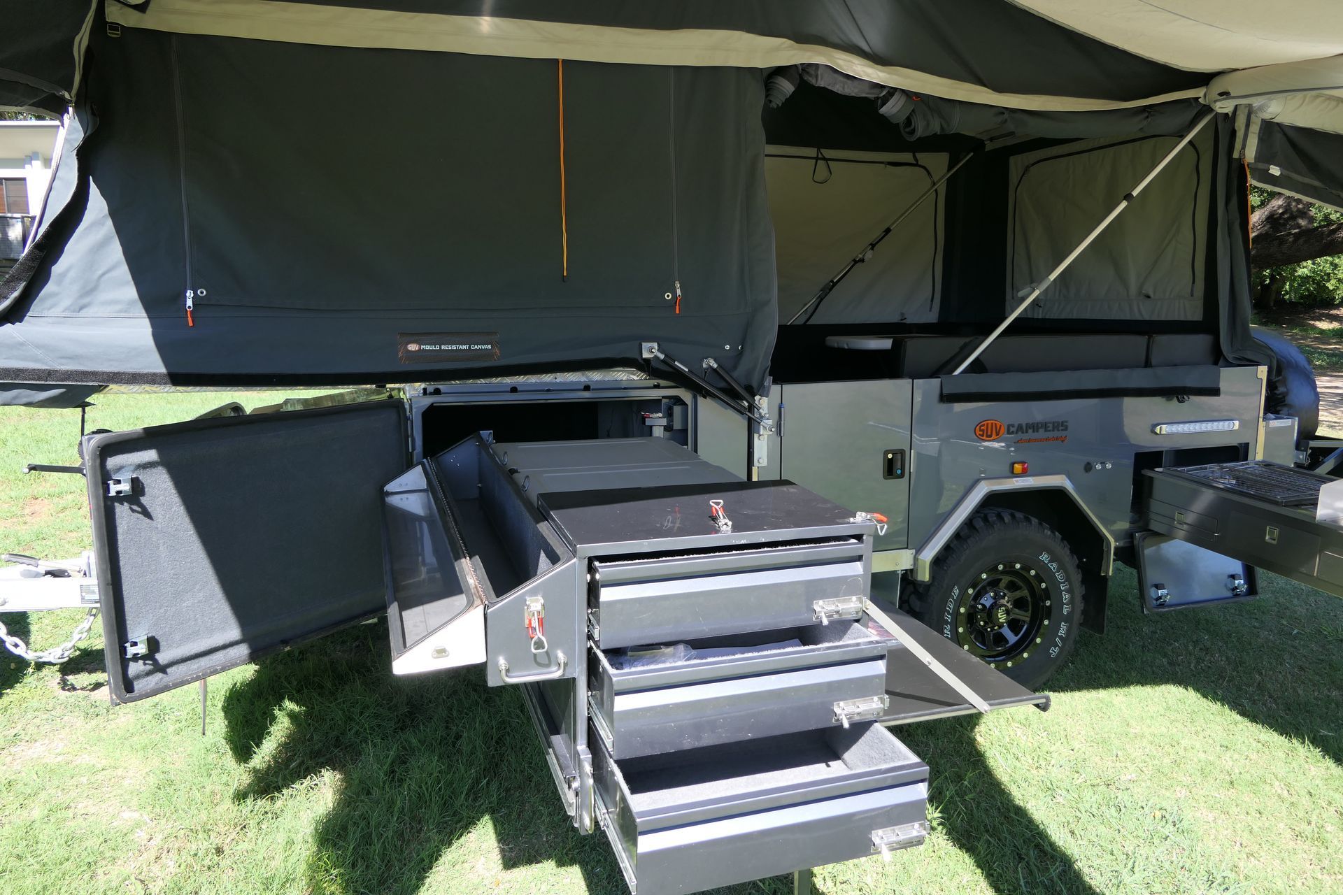 A trailer with a tent on top of it is parked in the grass.