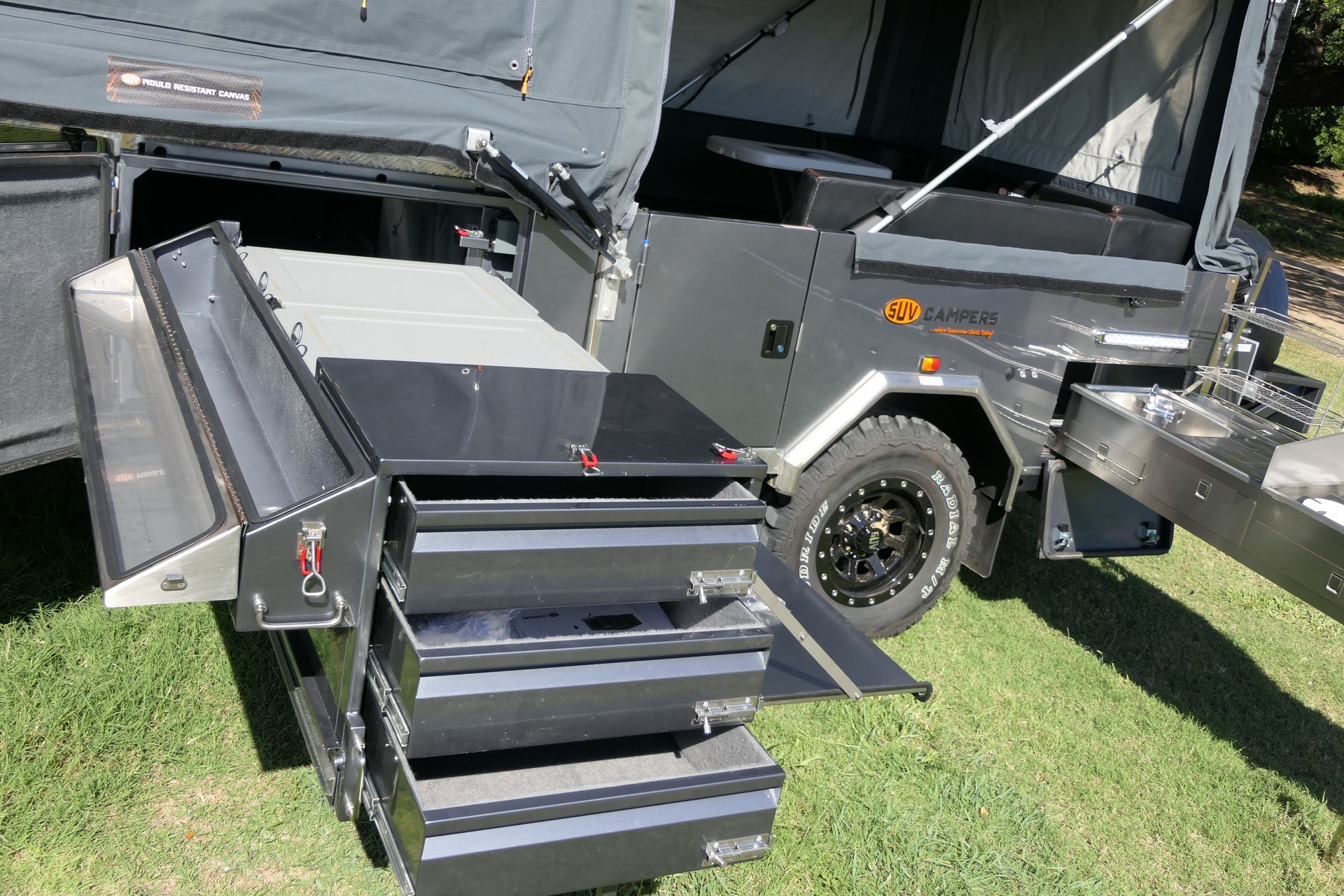 A camper trailer with its doors open is parked in the grass.