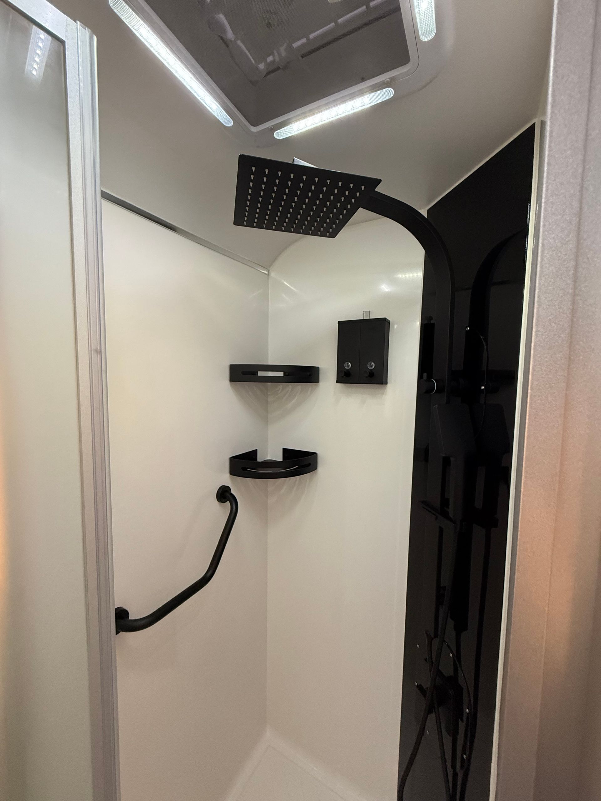 A shower with a black shower head and a black handle.