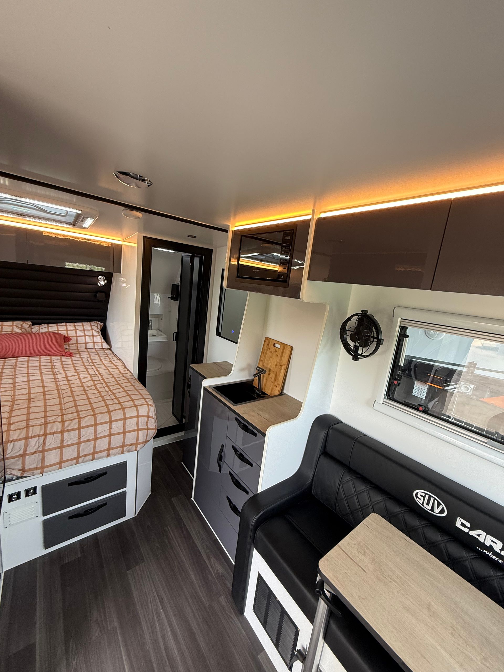 The inside of a camper with a bed , couch , table and cabinets.