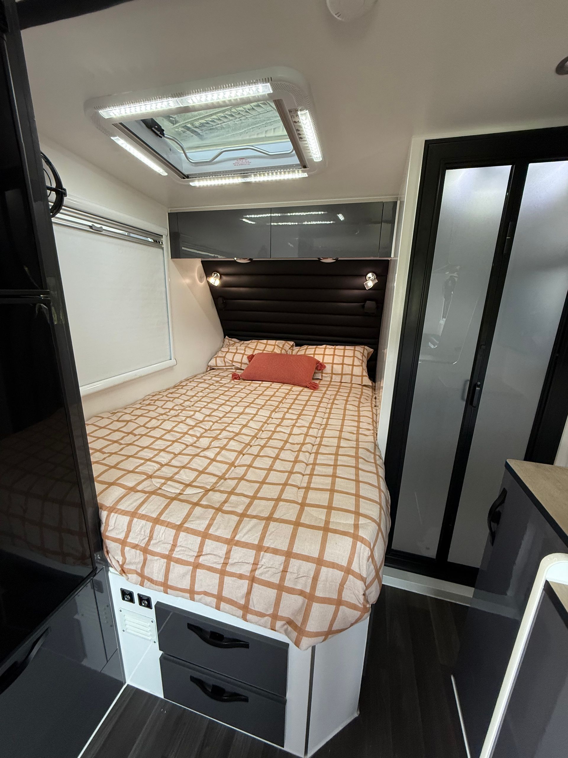 A bedroom in a camper with a bed and a skylight.