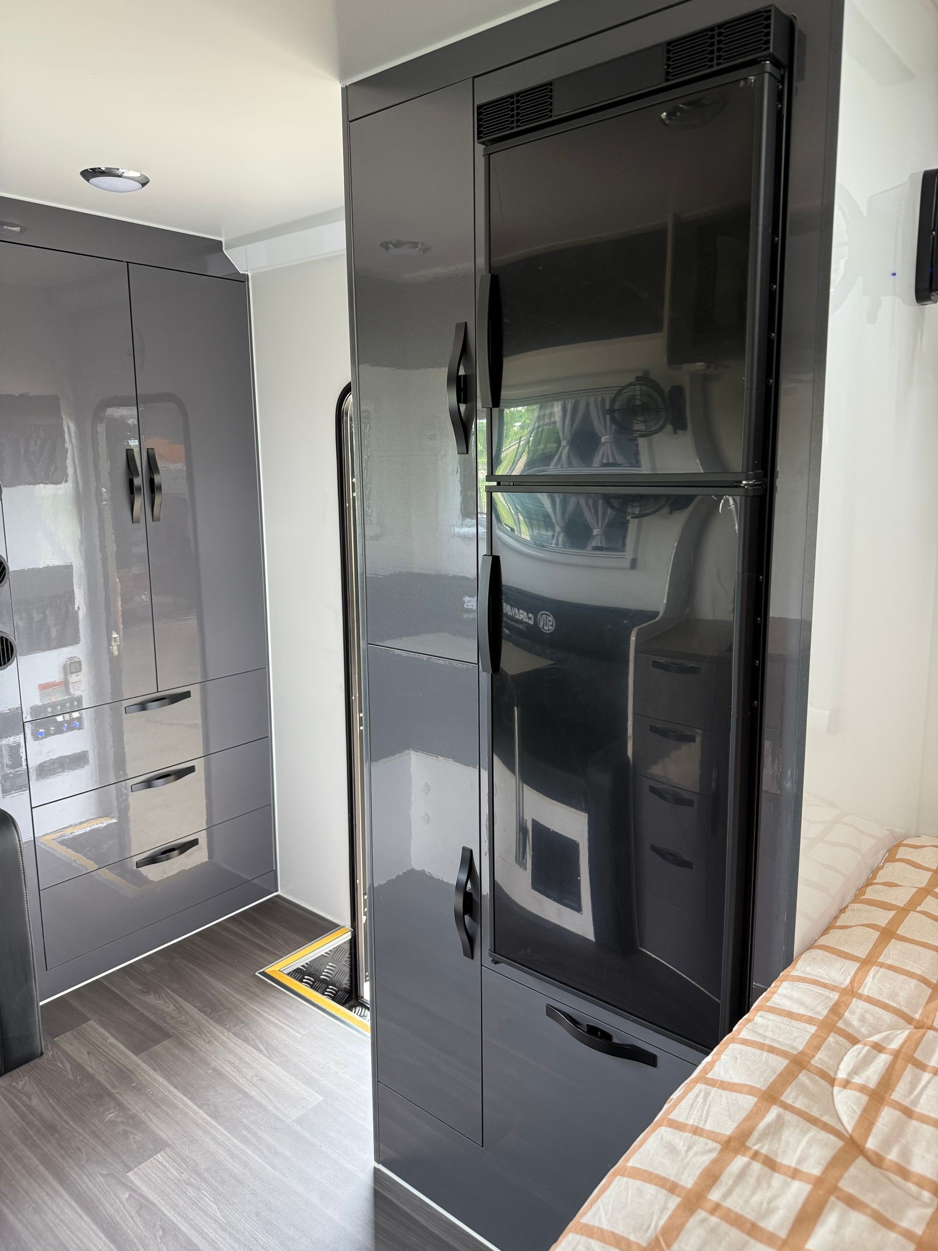 A black refrigerator is sitting in a room next to a bed.