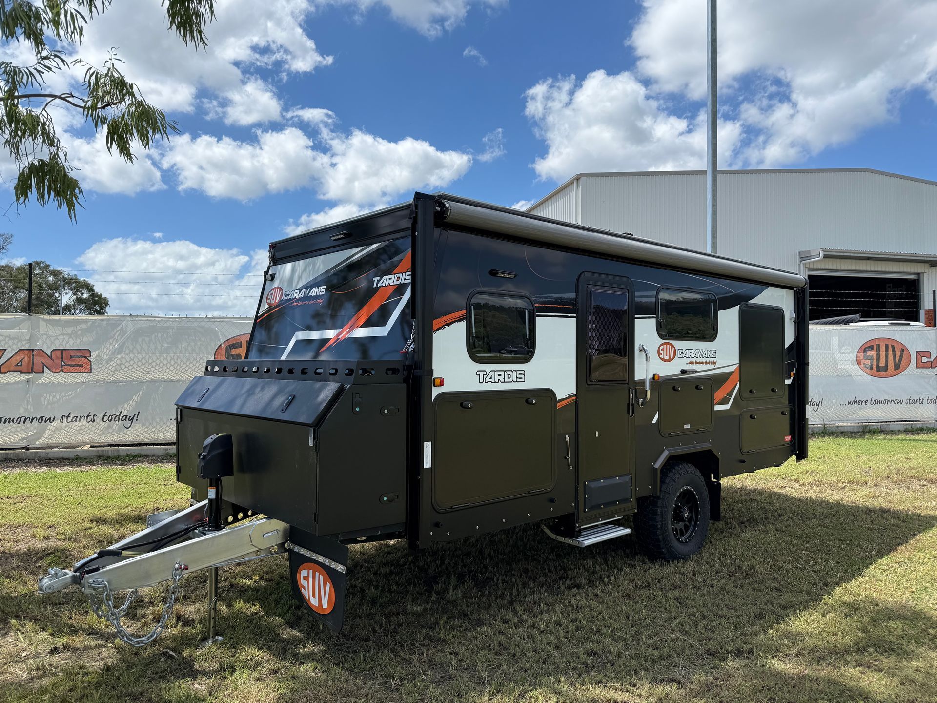 A camper trailer is parked in the grass in front of a building.
