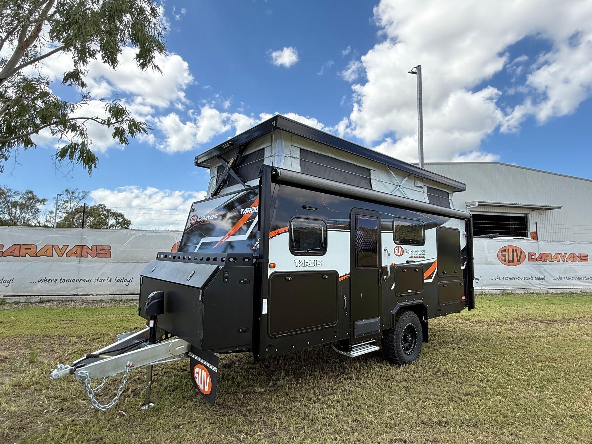 A black and white trailer is parked in a grassy field in front of a building.