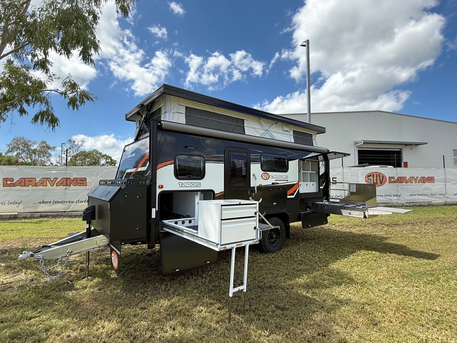 A camper trailer is parked in a grassy field in front of a building.