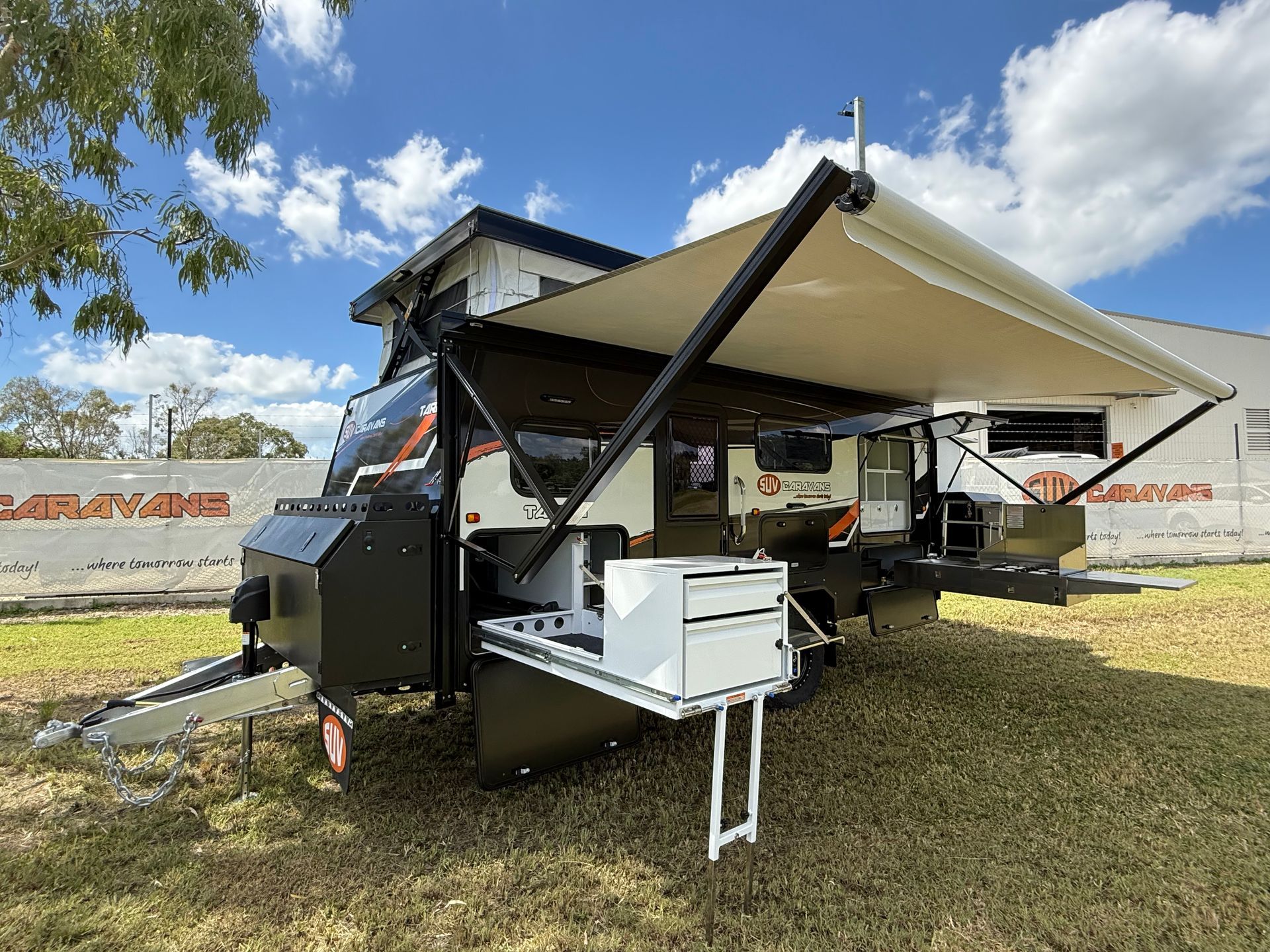 A camper trailer with a large awning is parked in a grassy field.