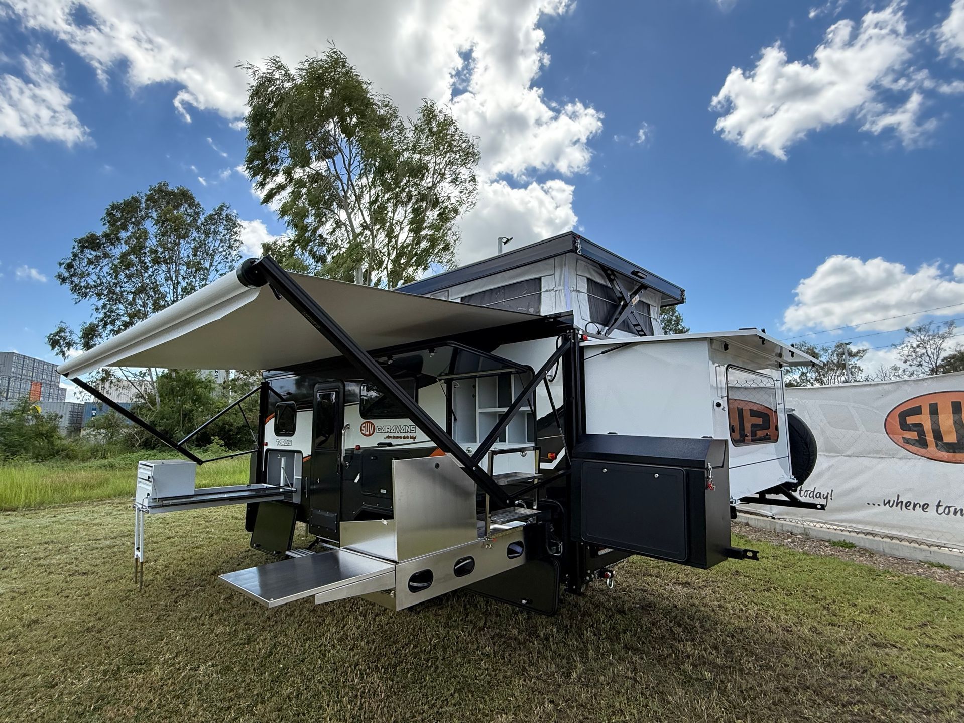 A trailer with an awning on top of it is parked in a grassy field.