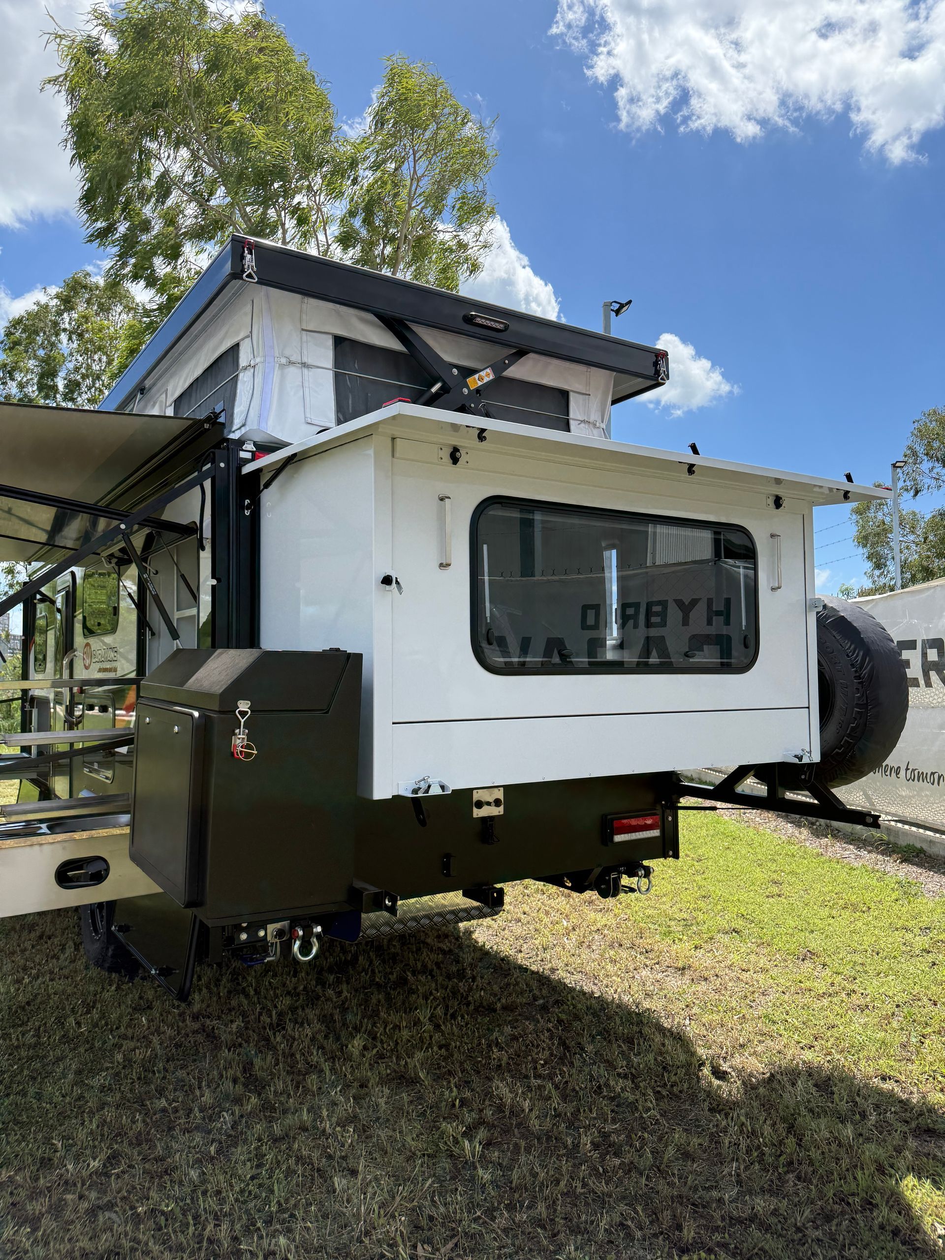 A white trailer with a tent on top of it is parked in the grass.