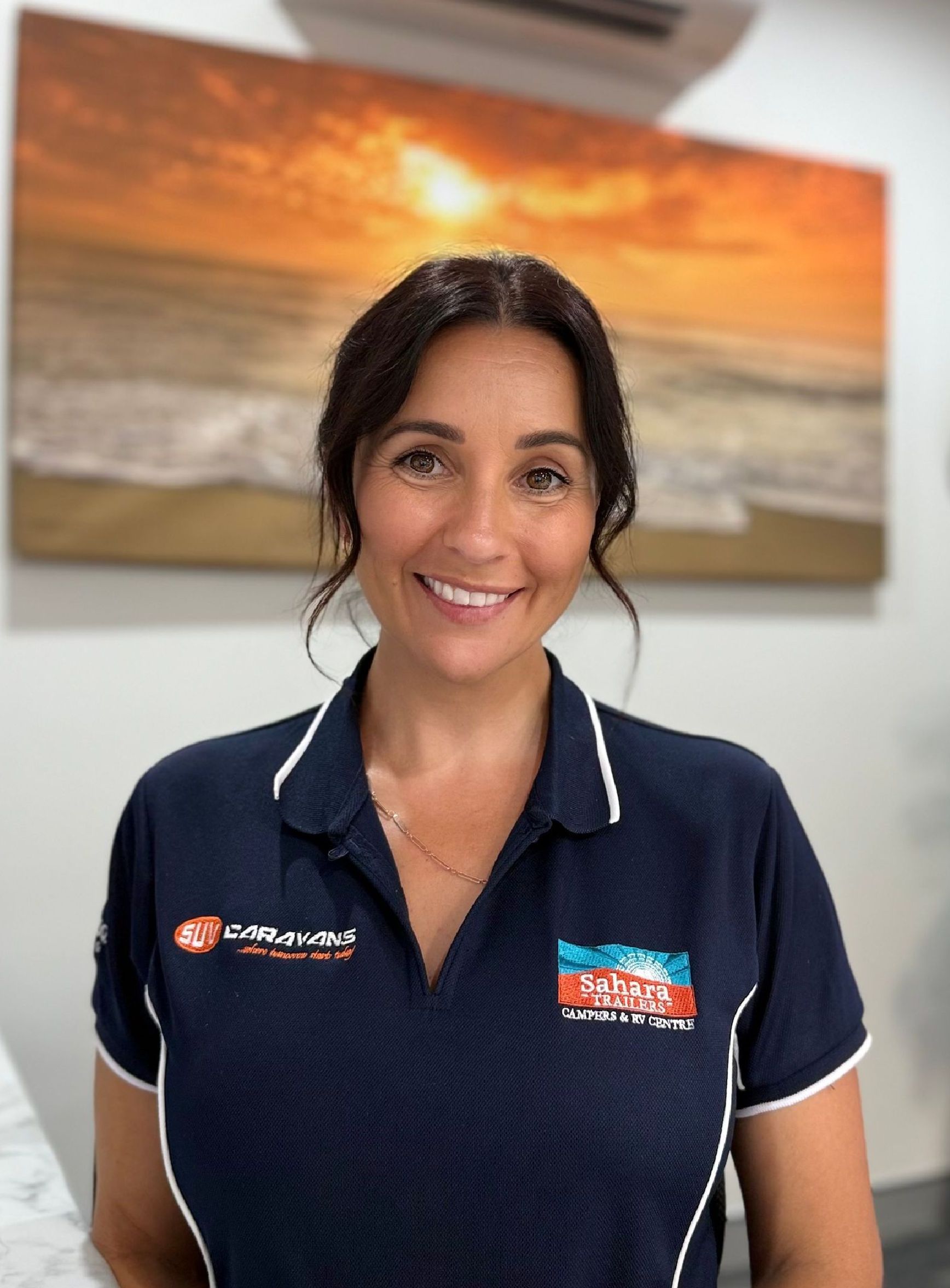 A woman in a blue shirt is smiling in front of a painting of the ocean.