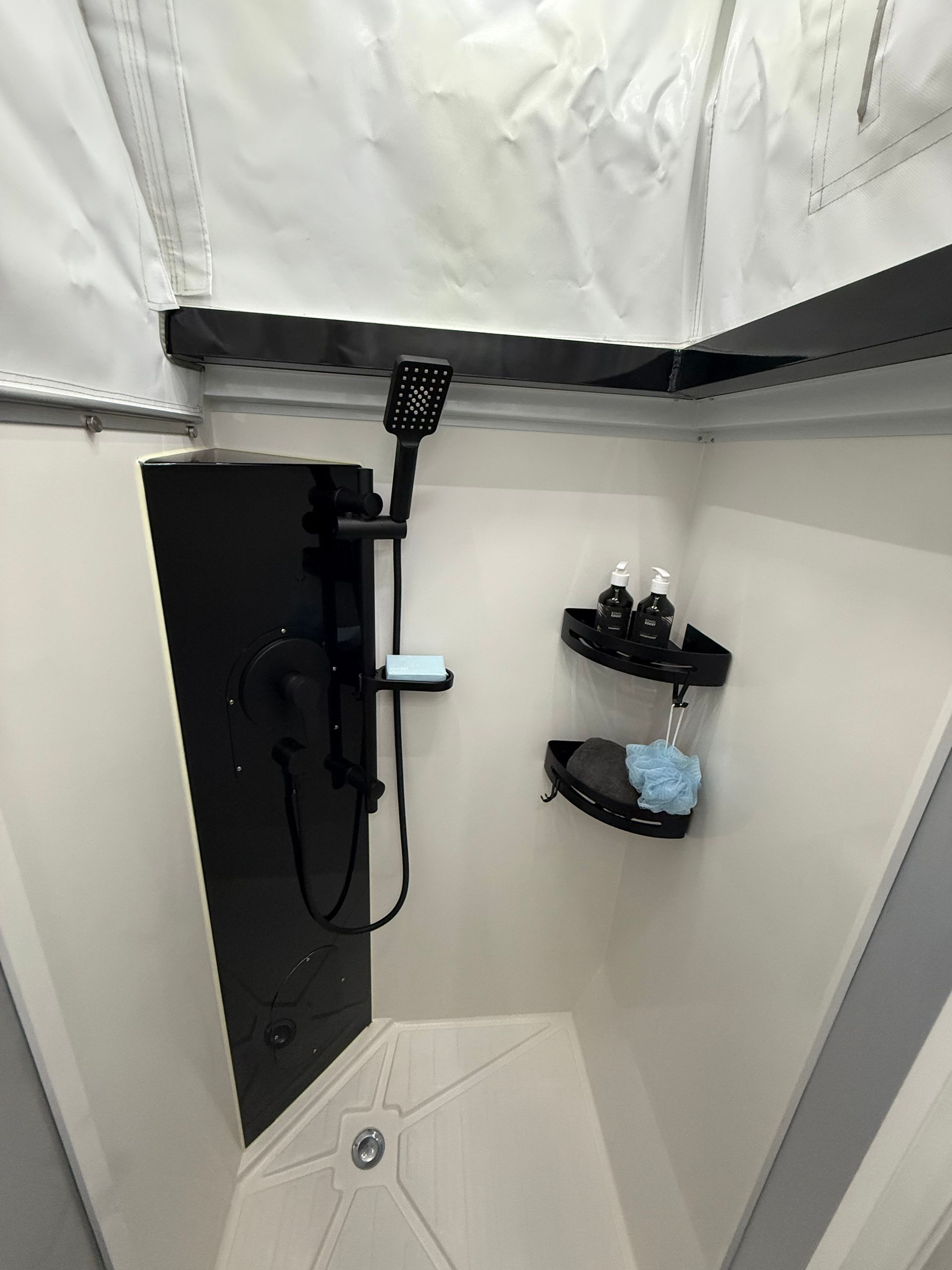 A shower with a black shower head and a black curtain hanging from the ceiling.